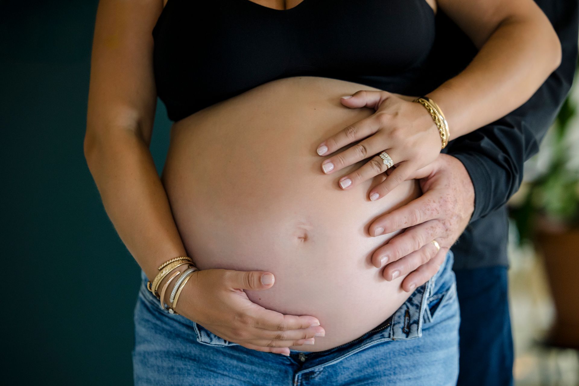 Pregnant belly with two hands gently resting on it, wearing a black top and jeans