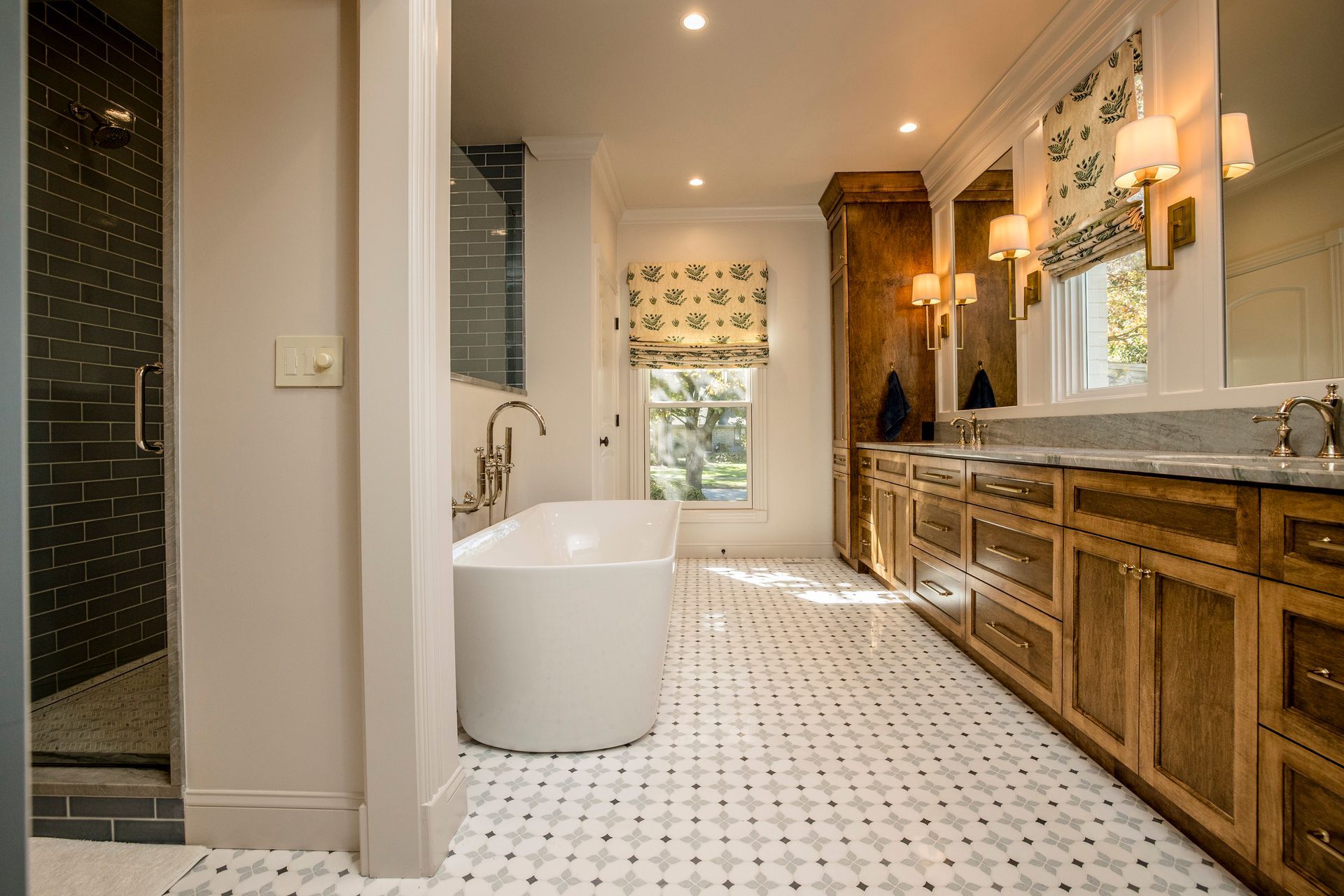 Bright bathroom with a white tub, wooden vanity, mosaic floor, and shower enclosure