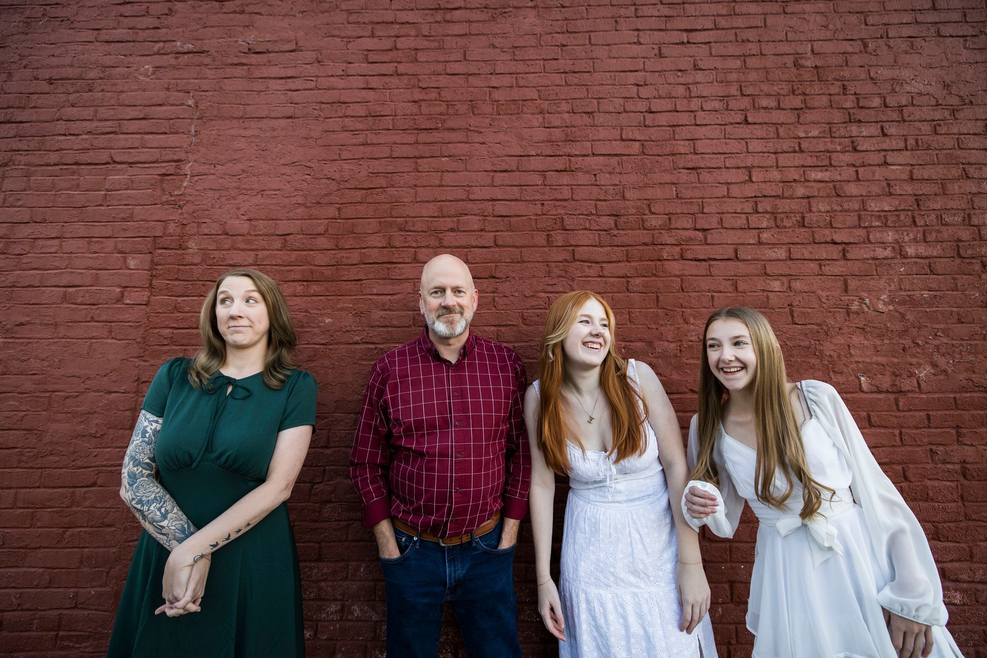 Four people standing against a red brick wall, smiling and posing together.