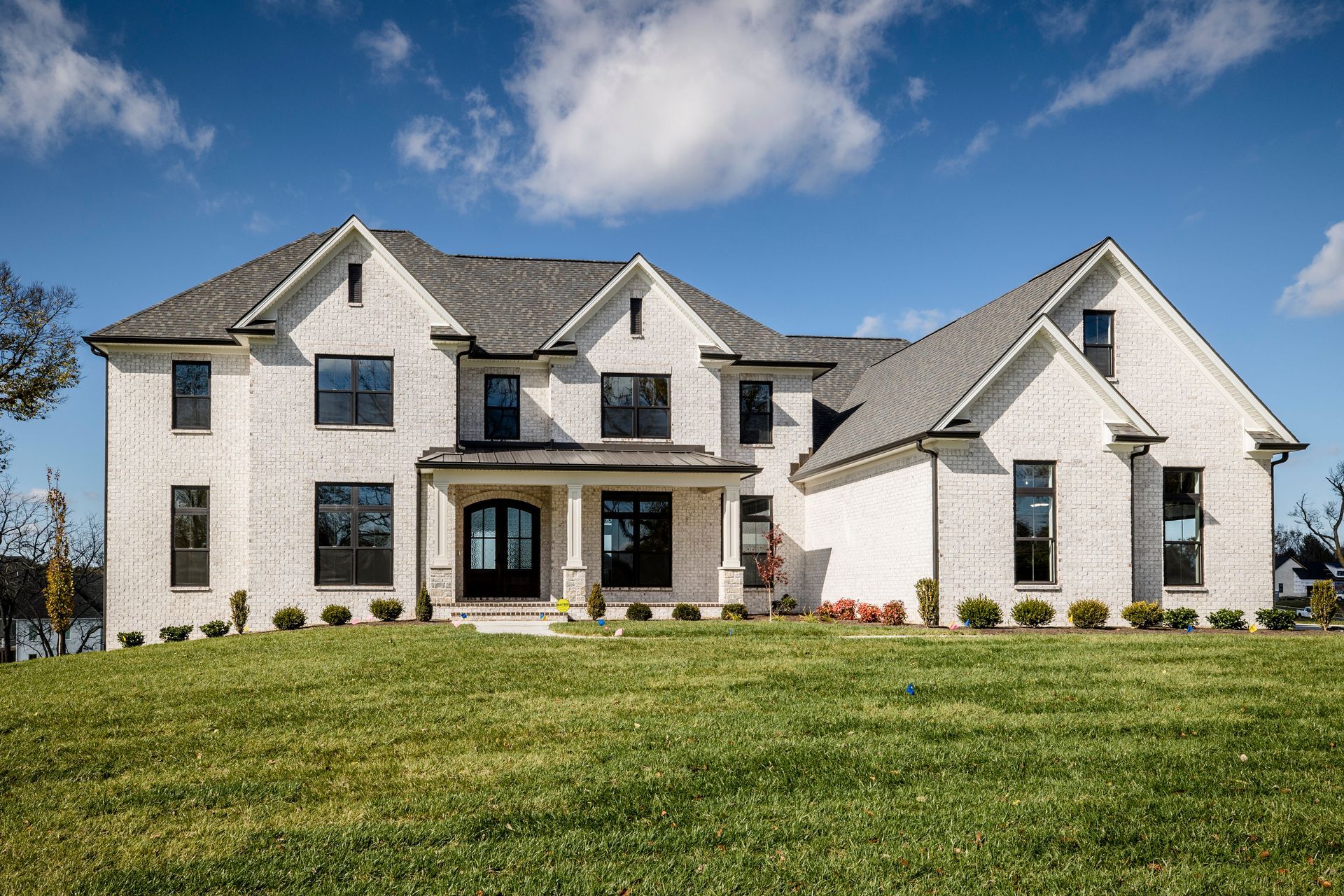 Large two-story stone house with gray roof and manicured lawn under a blue sky