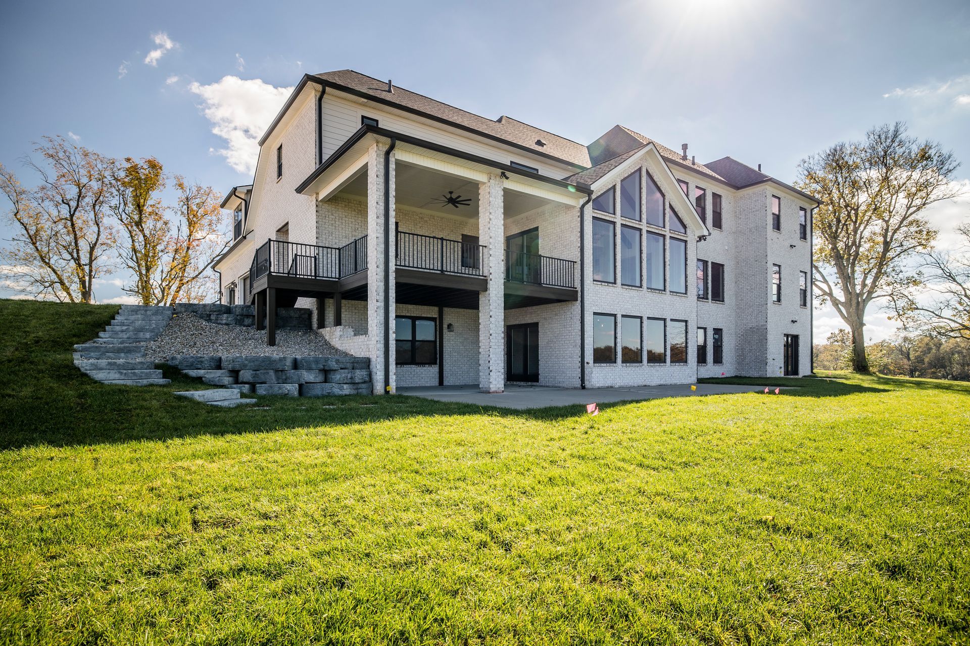 Large white house with covered porch on a sunny lawn, viewed from the yard