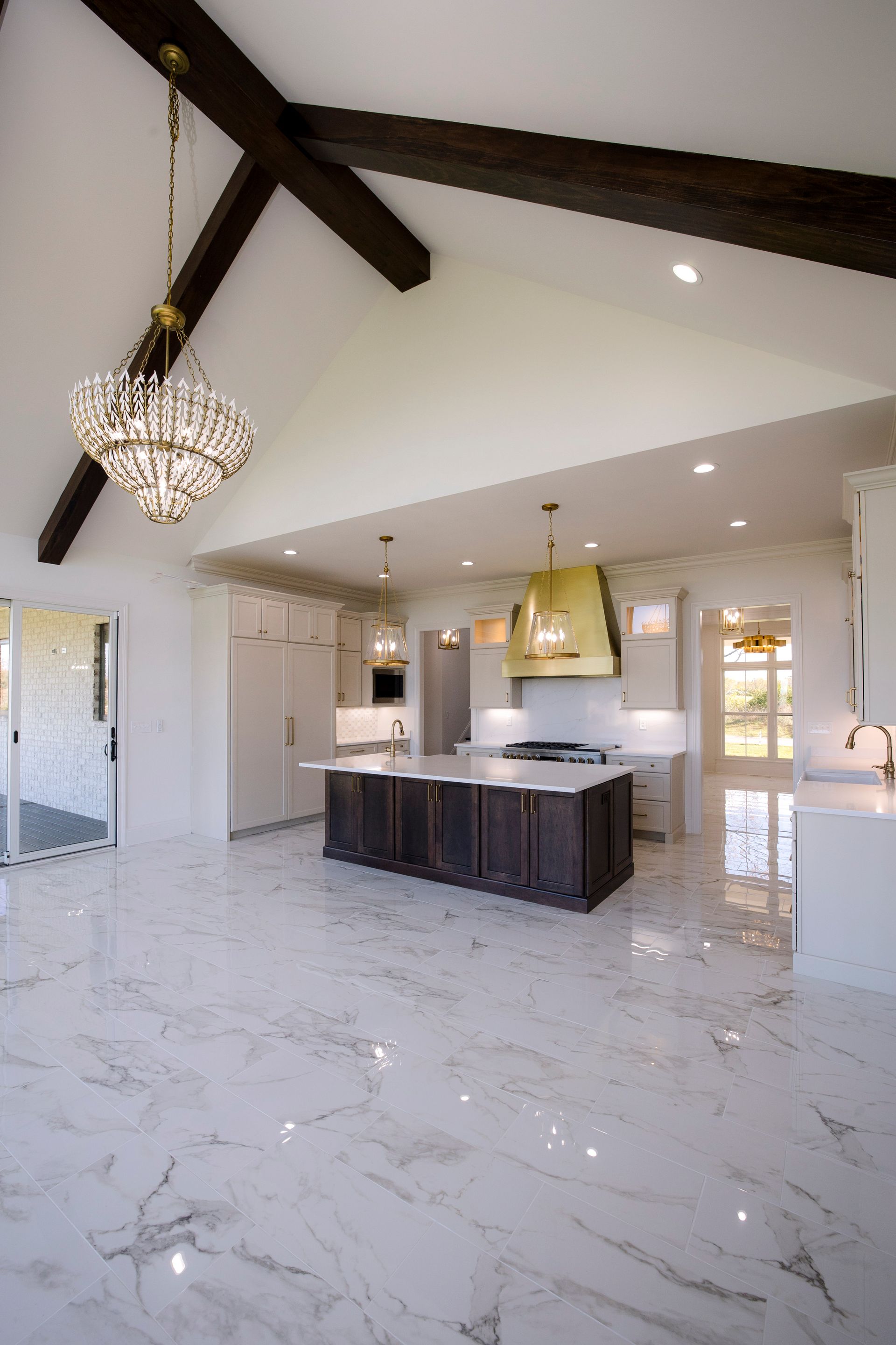 Spacious modern kitchen with marble floors, dark wood beams, white cabinets, and a central island