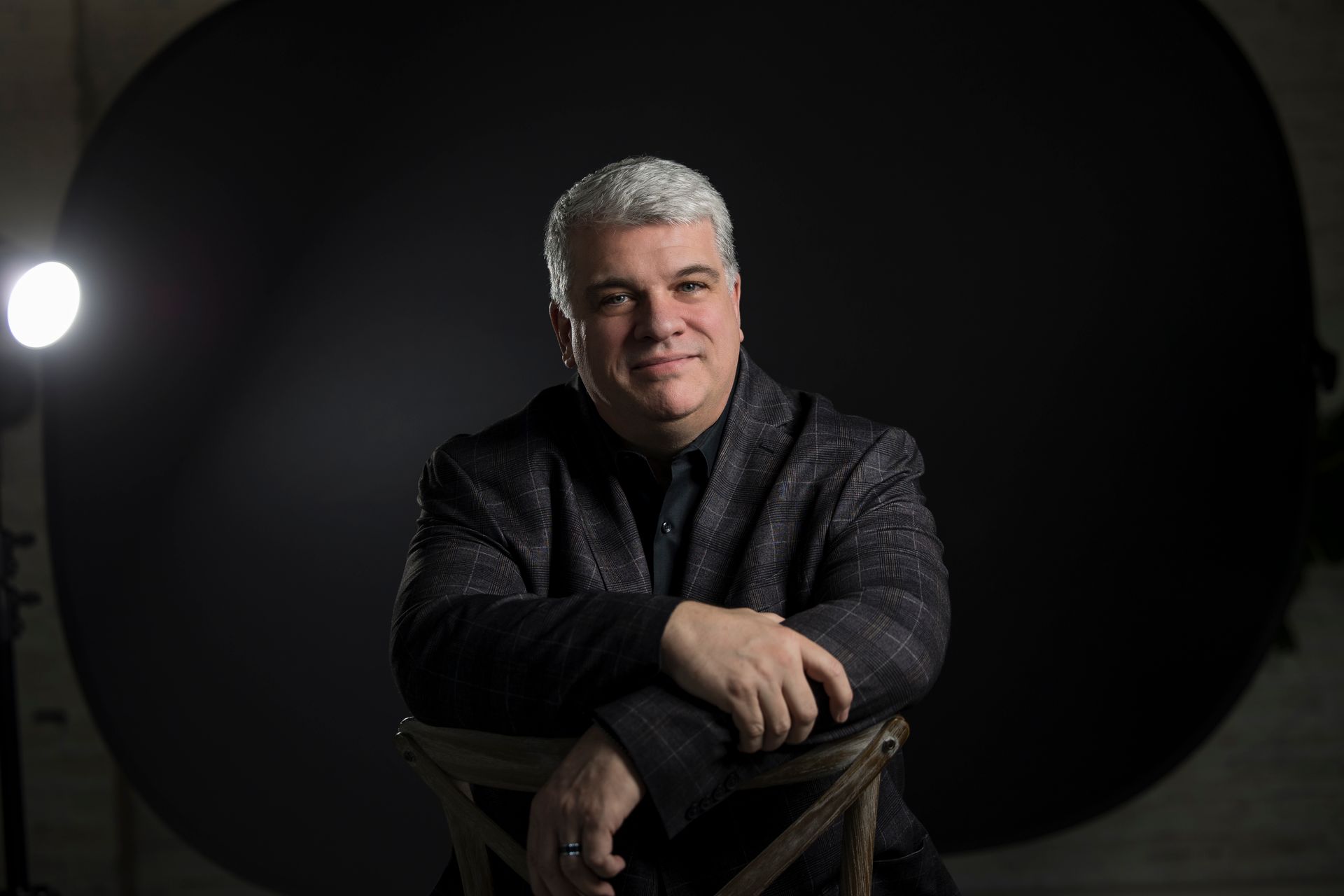 Portrait of a smiling man with folded arms against a dark studio backdrop