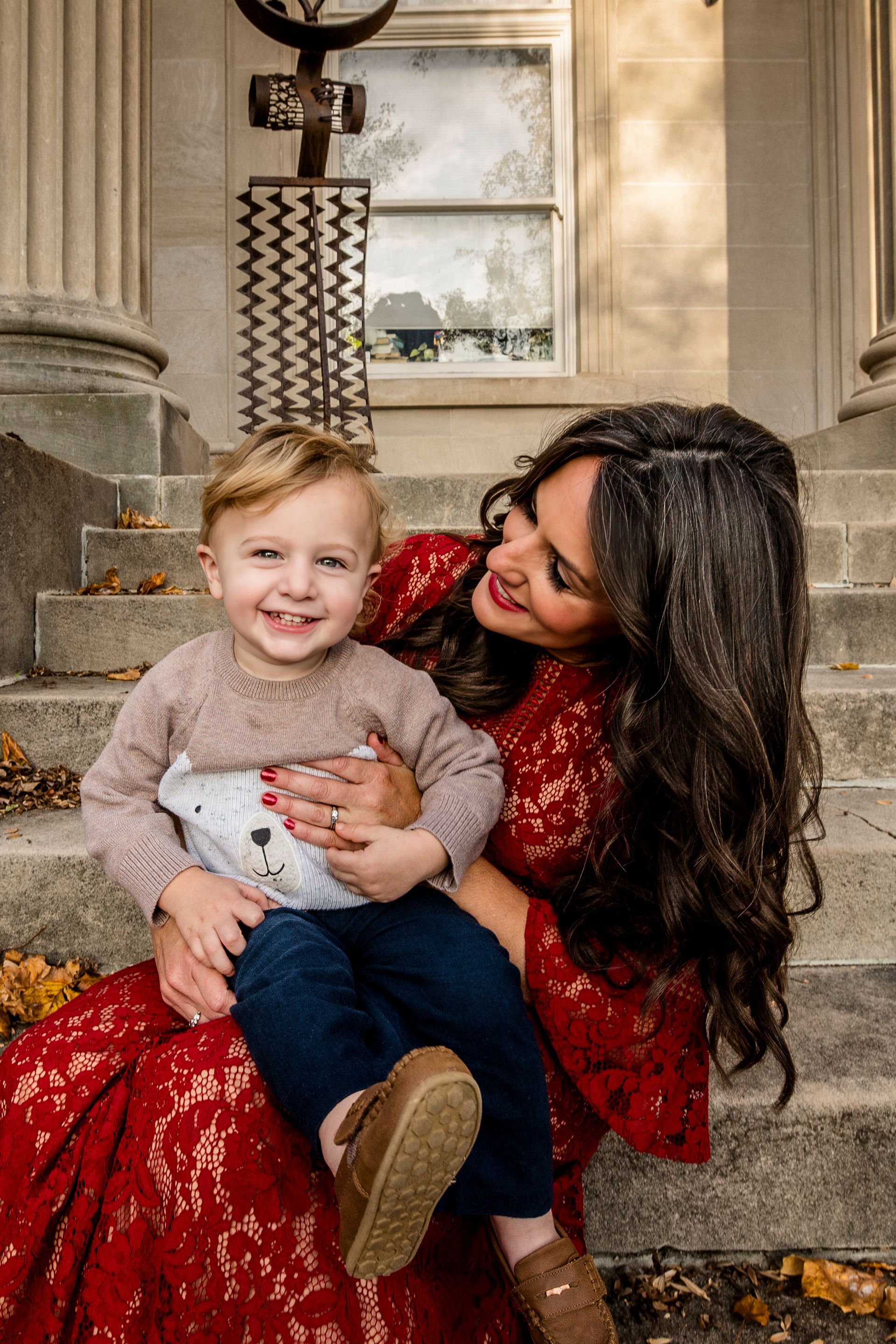 Woman in a red dress holding a smiling child on stone steps outside a building