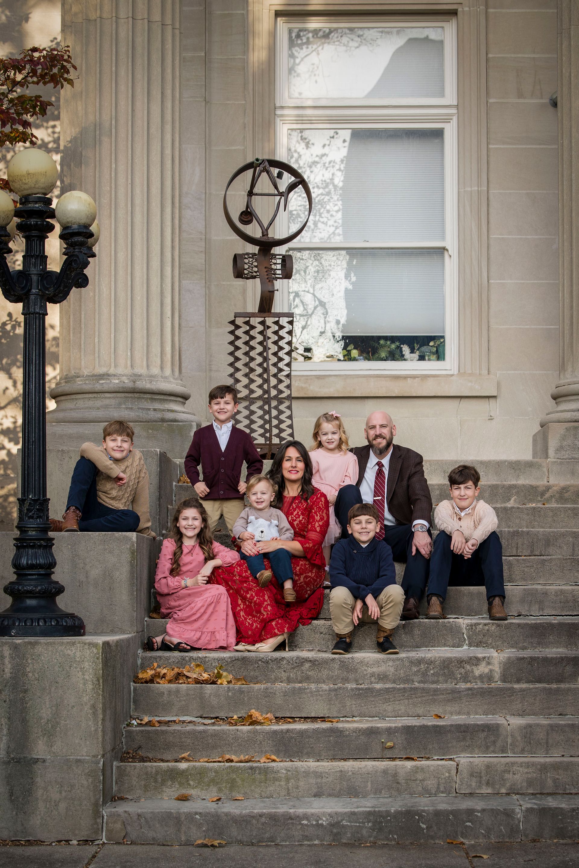 Group posed on stone steps outside a building, with a decorative lamp post and window behind them.