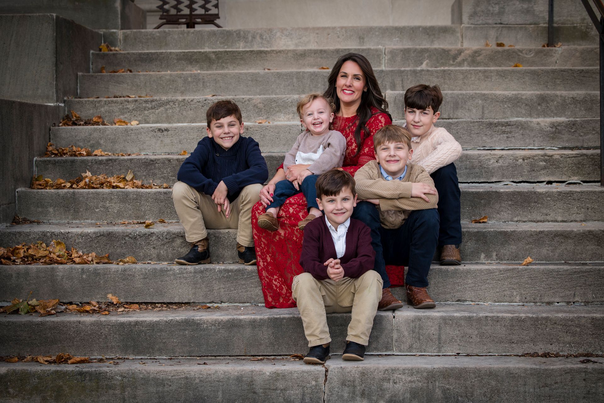 Family seated on concrete steps, with a woman in a red dress surrounded by four children and one child in front.