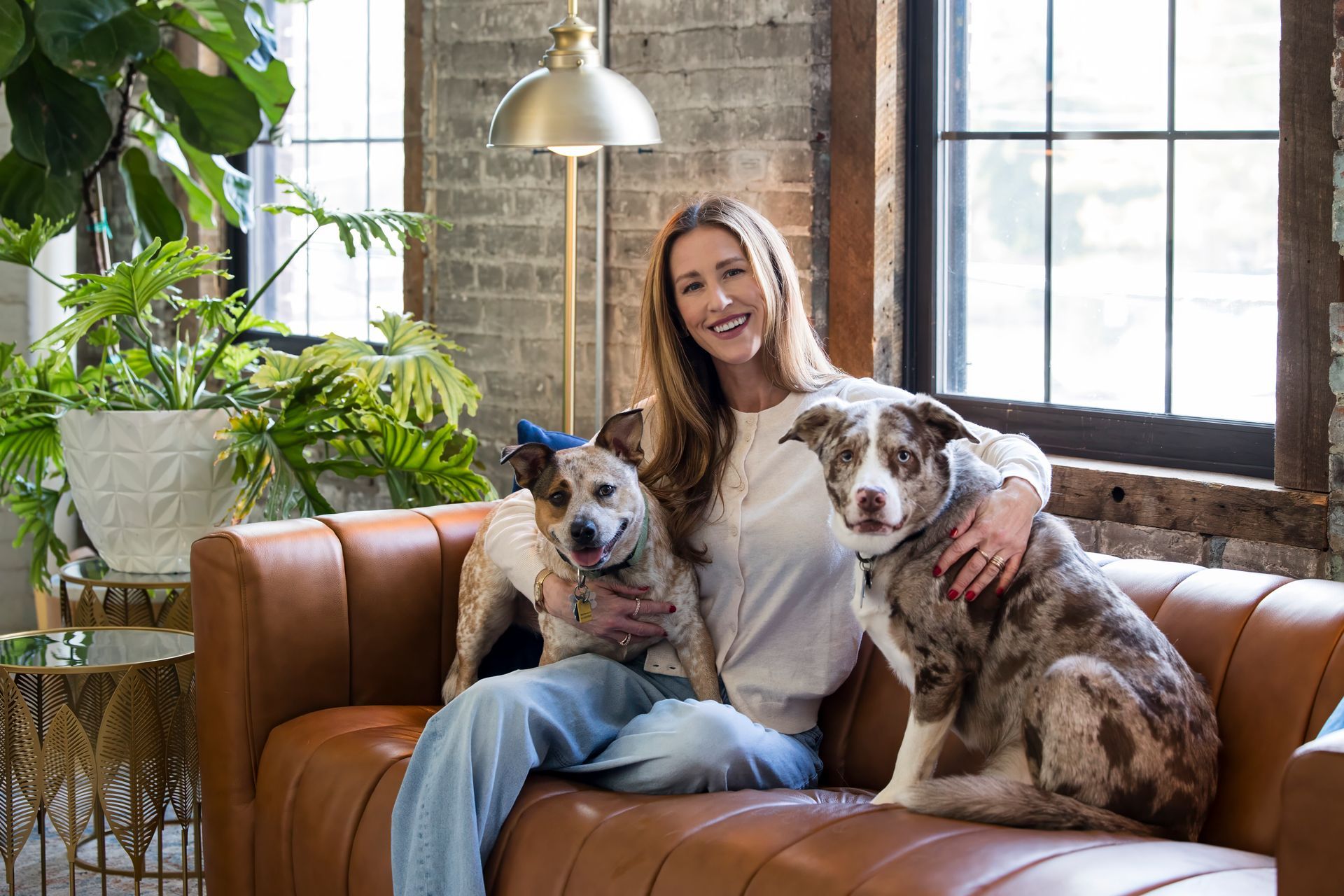 Woman sitting on a leather sofa with two spotted dogs in a bright loft-style living room