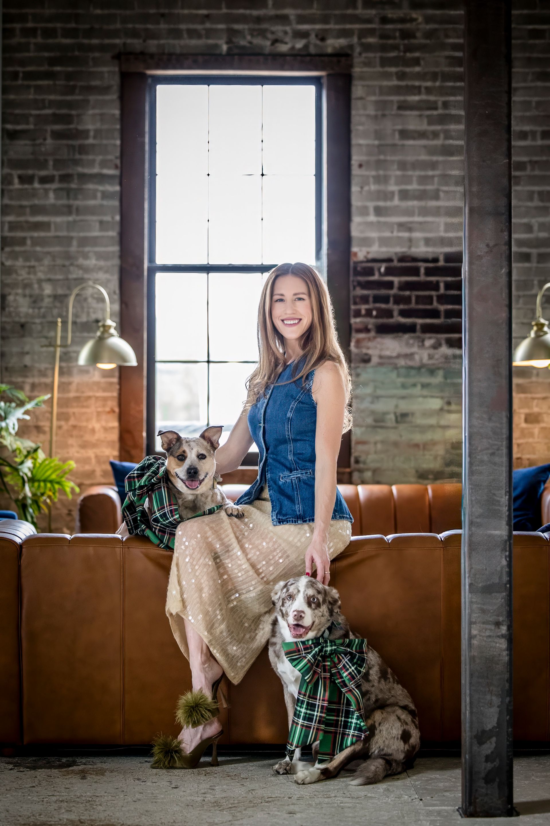 Woman seated on a tan couch with two small dogs in a brick loft living room