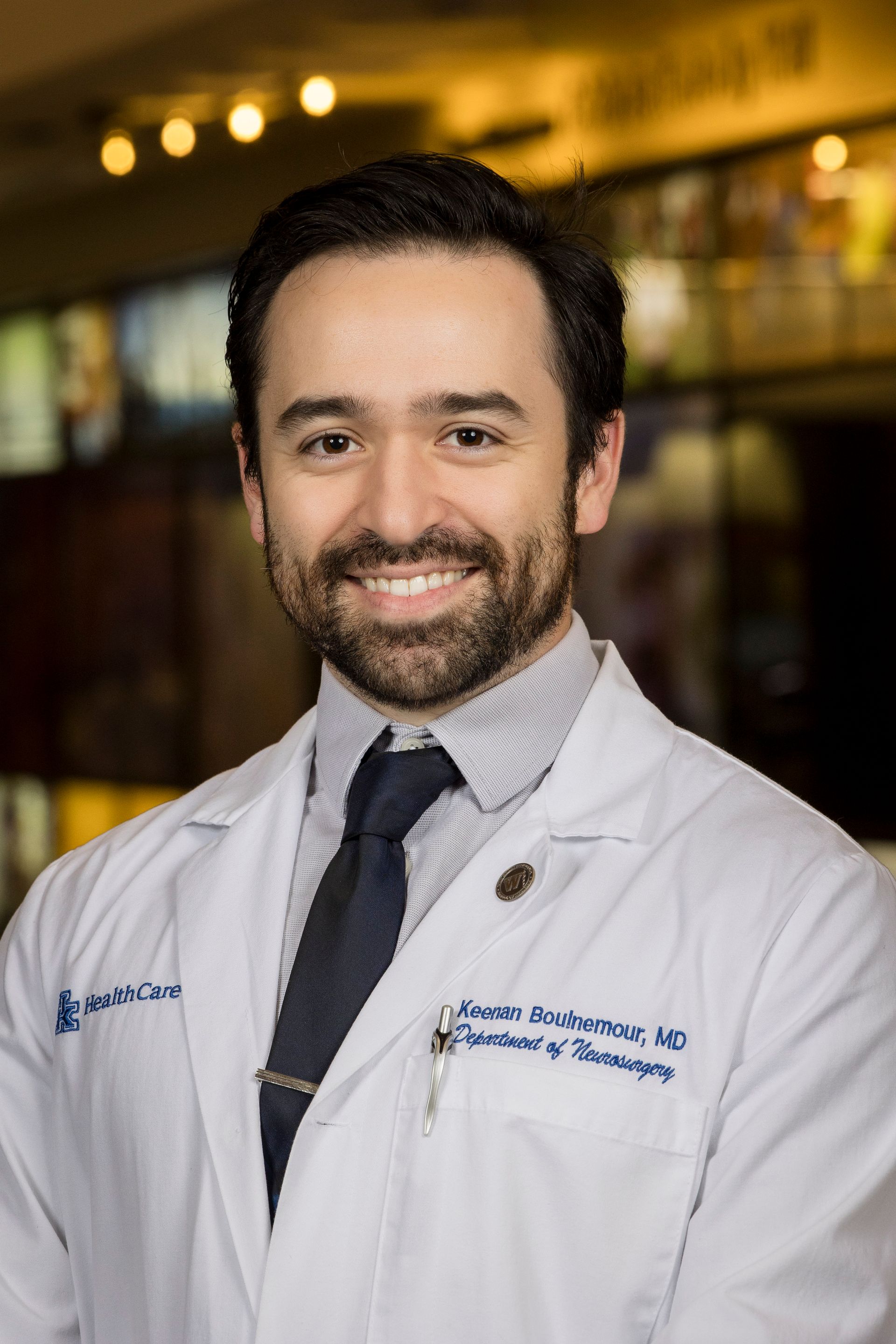 Smiling doctor in white coat and tie, standing in a warmly lit hospital setting
