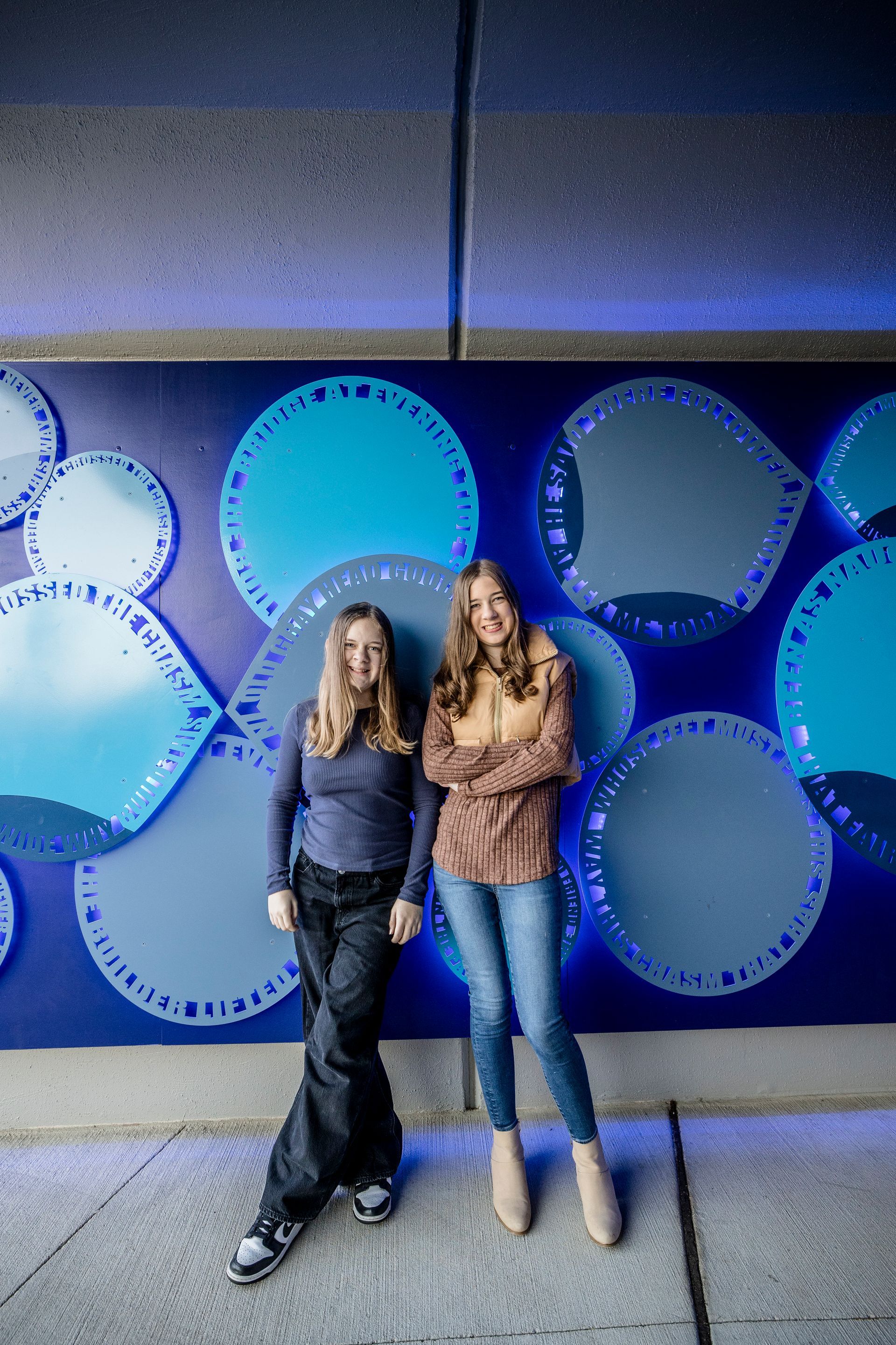 Two women standing in front of a blue wall with large circular patterns
