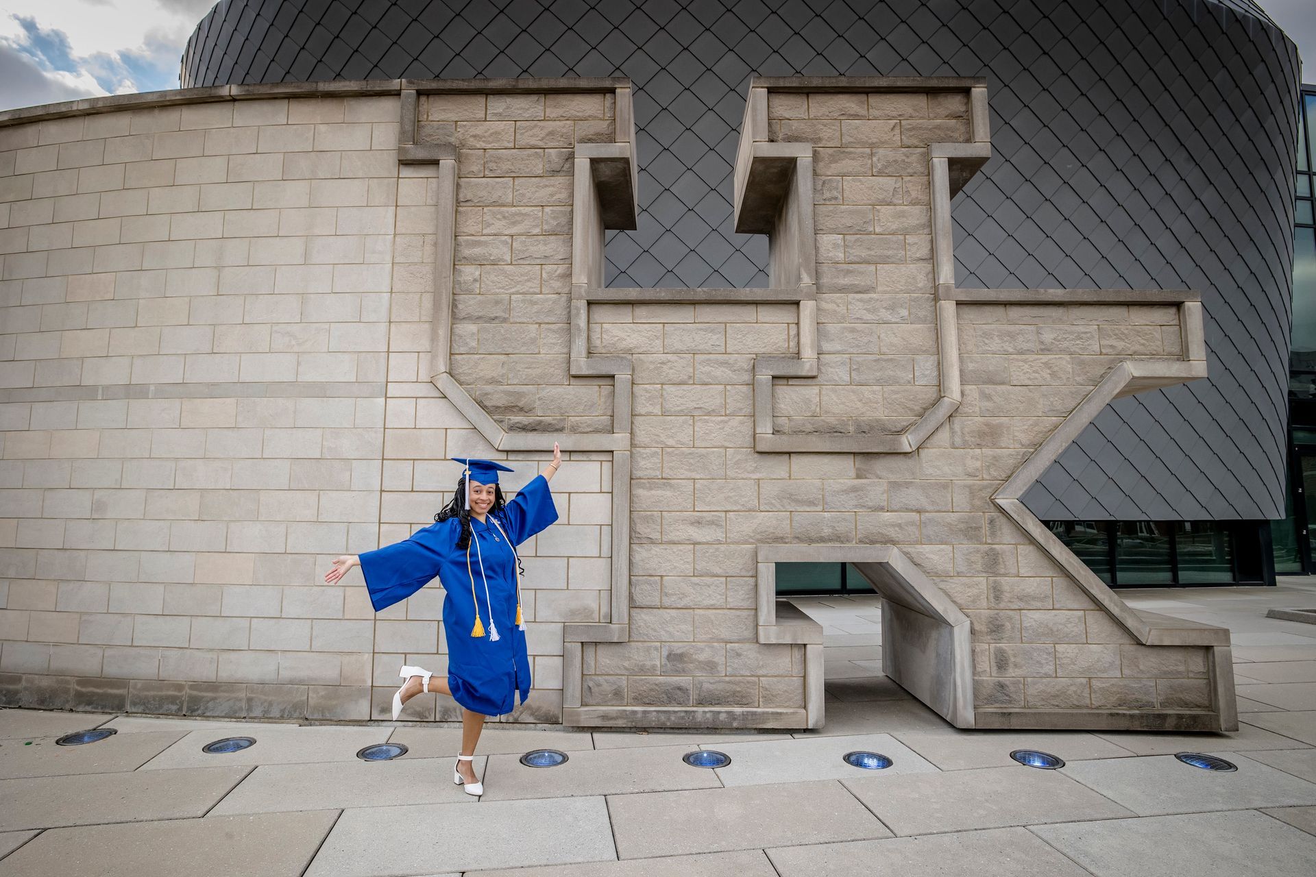 Person in a bright blue outfit posing in front of a large concrete wall sculpture outdoors.