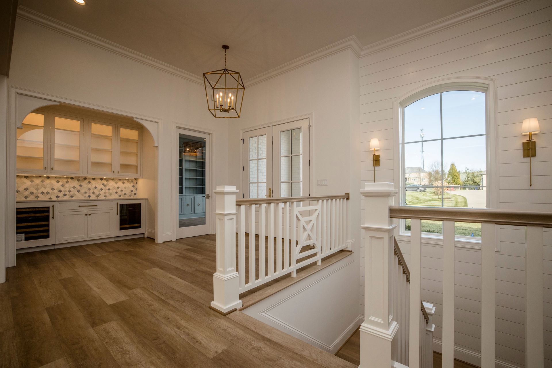 Bright foyer with white railings, wood floors, arched opening, and large window overlooking outside