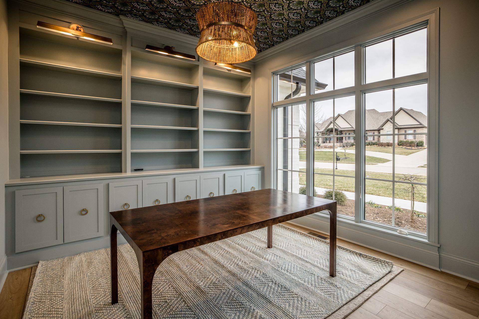 Home office with built-in shelves, a wooden desk, and large windows overlooking a yard