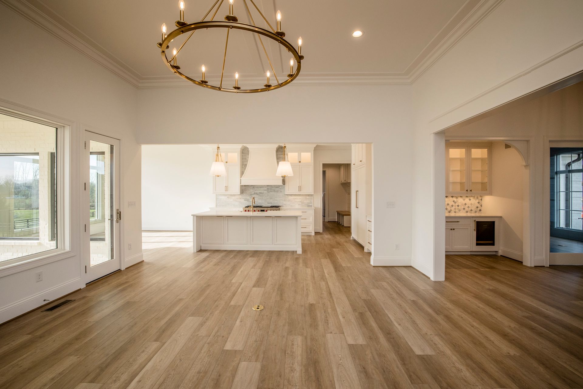 Spacious empty living room with hardwood floors, white walls, chandelier, and open kitchen beyond