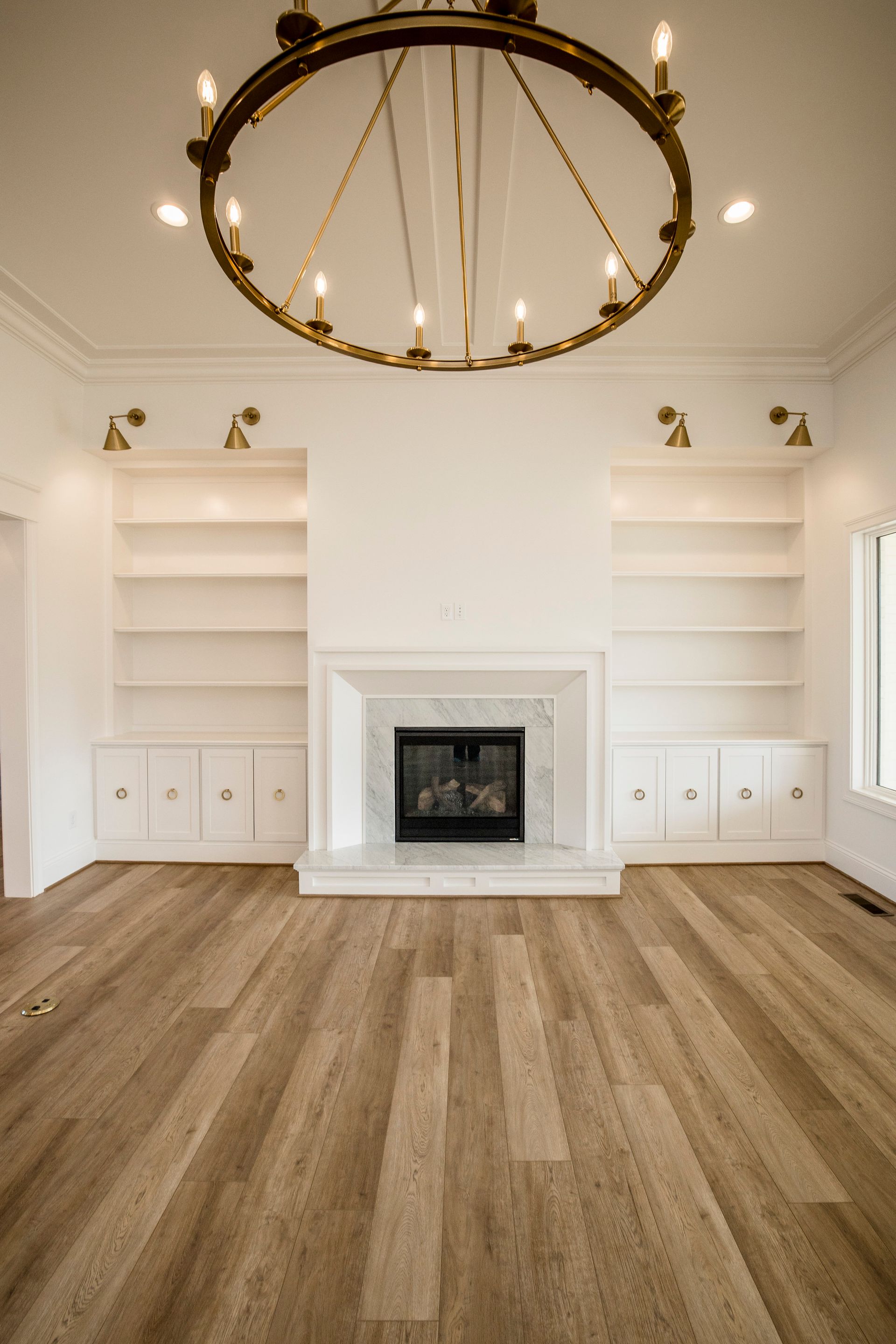 Bright living room with white built-ins, a fireplace, wood floors, and a large gold chandelier.