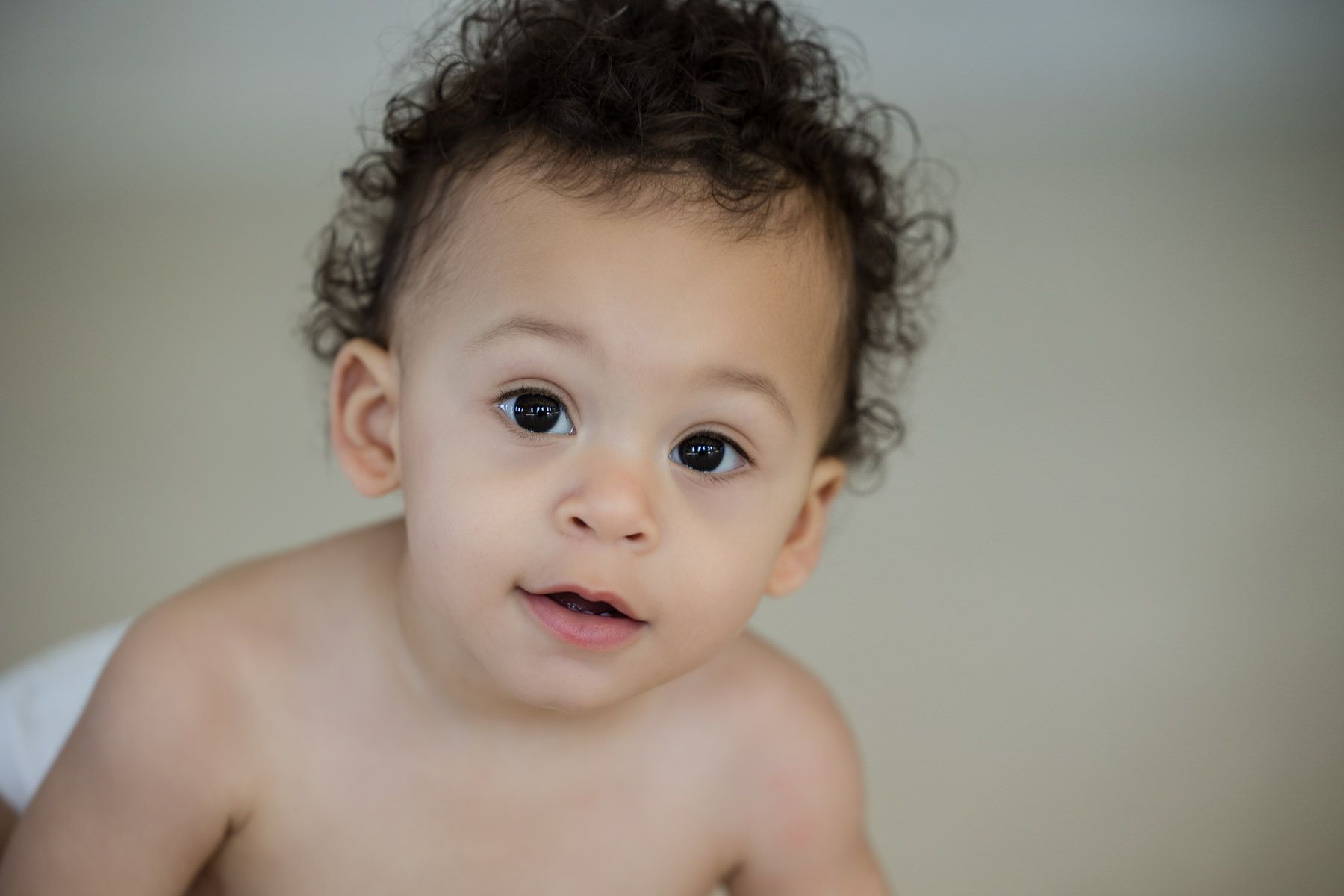 Curious baby with curly hair looking at the camera against a soft blurred background