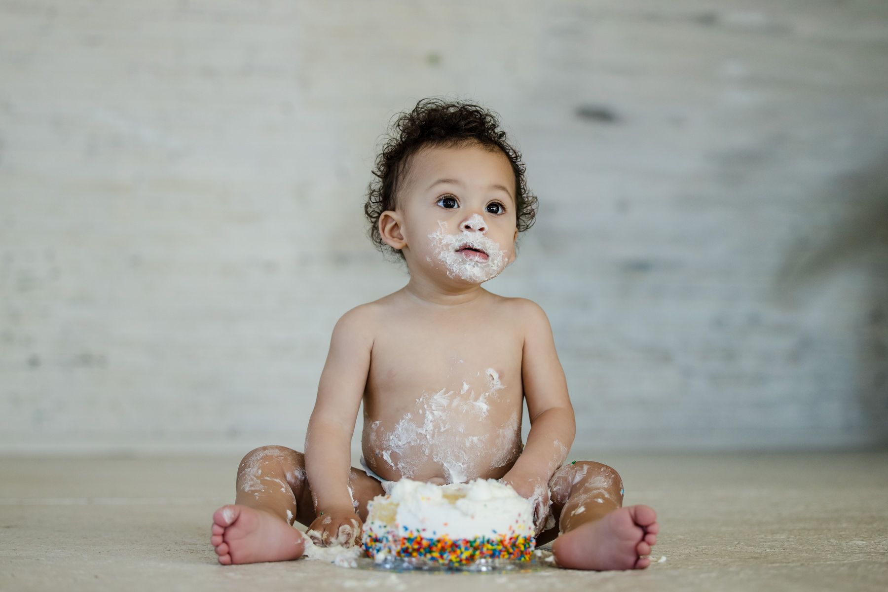Toddler sitting on the floor, covered in cake frosting, with a smashed cake in front of them.