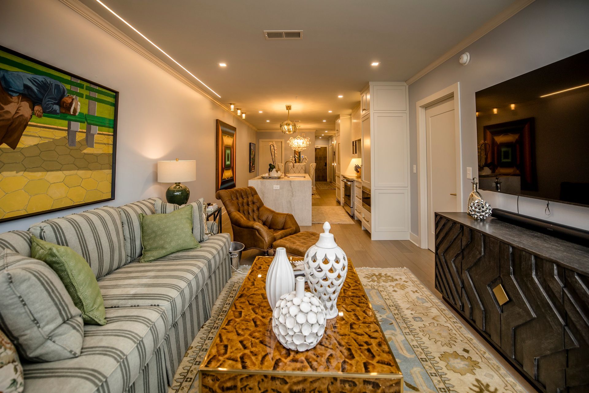 Bright living room with striped sofa, patterned coffee table, wall art, and a hallway opening to a kitchen.