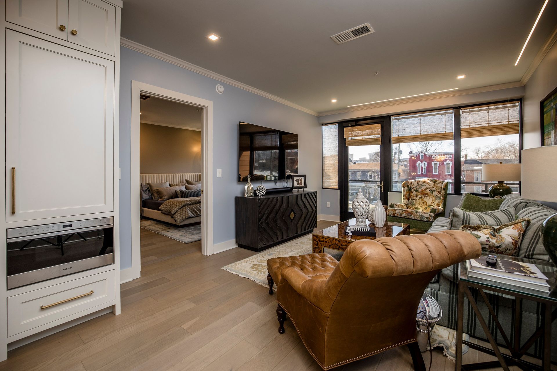Modern open-concept living room with leather chair, sofa, TV, and large windows
