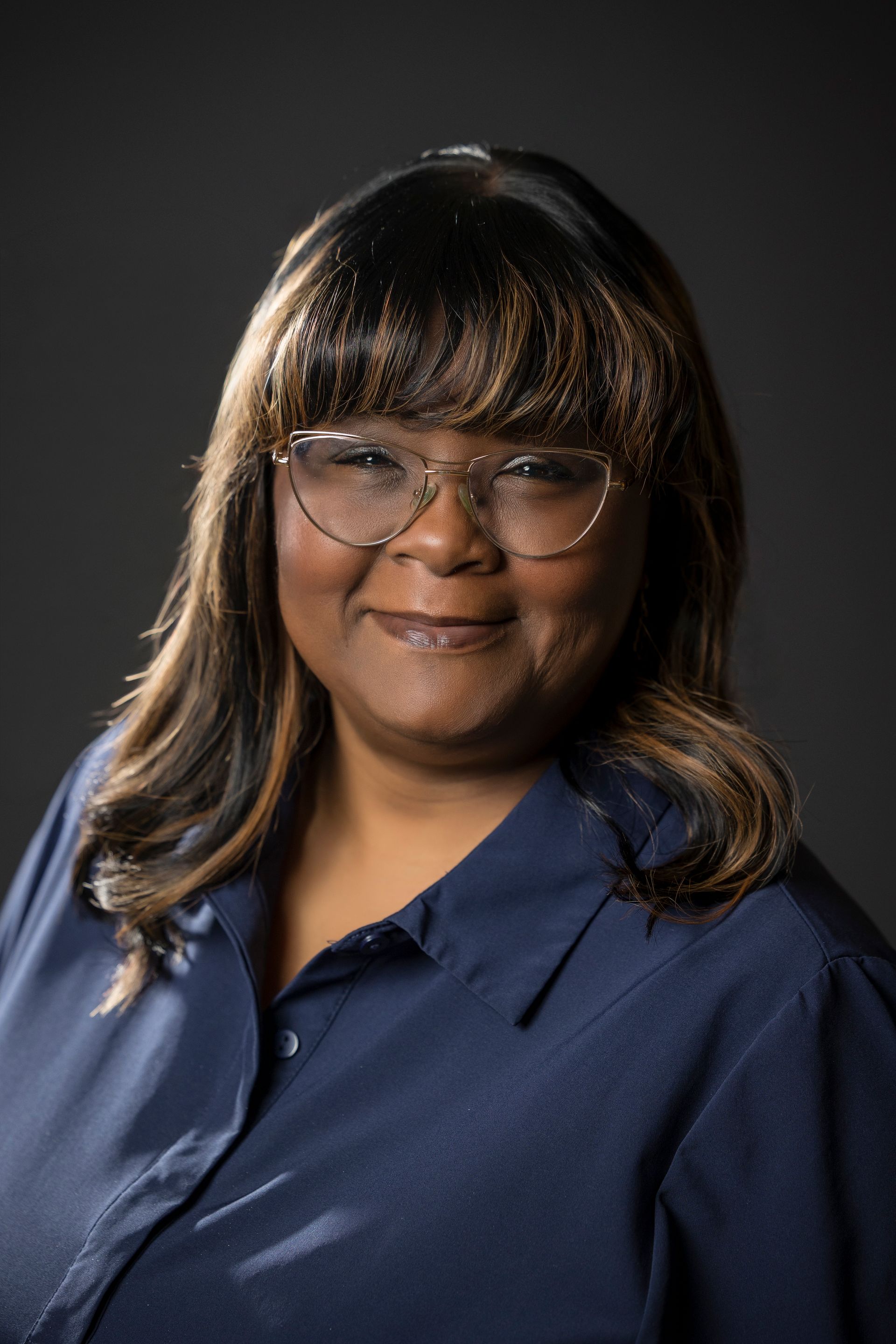 Studio portrait of a smiling person in glasses and a navy shirt against a dark background