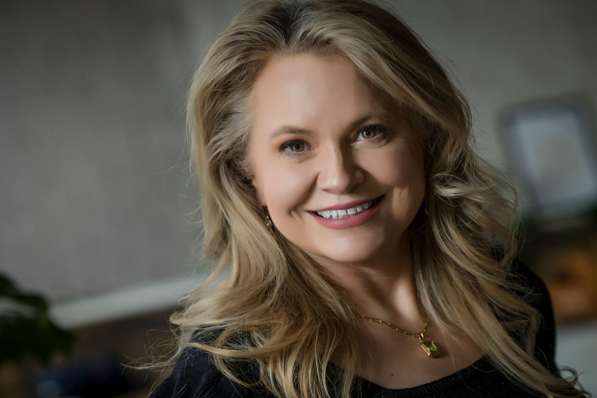 Smiling blonde woman in a black top against a softly blurred indoor background