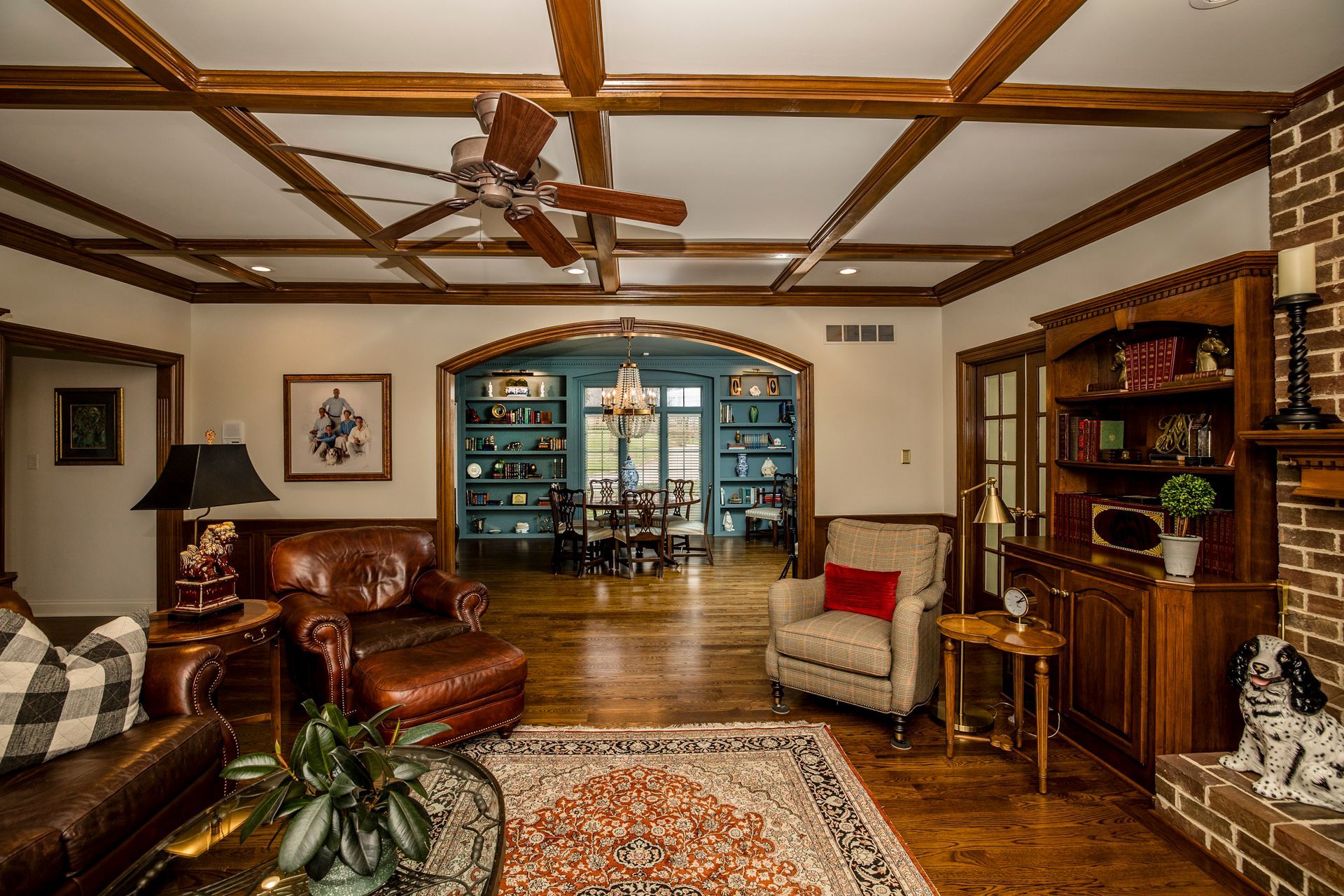 Cozy living room with leather chairs, wooden ceiling beams, patterned rug, and blue built-in shelves