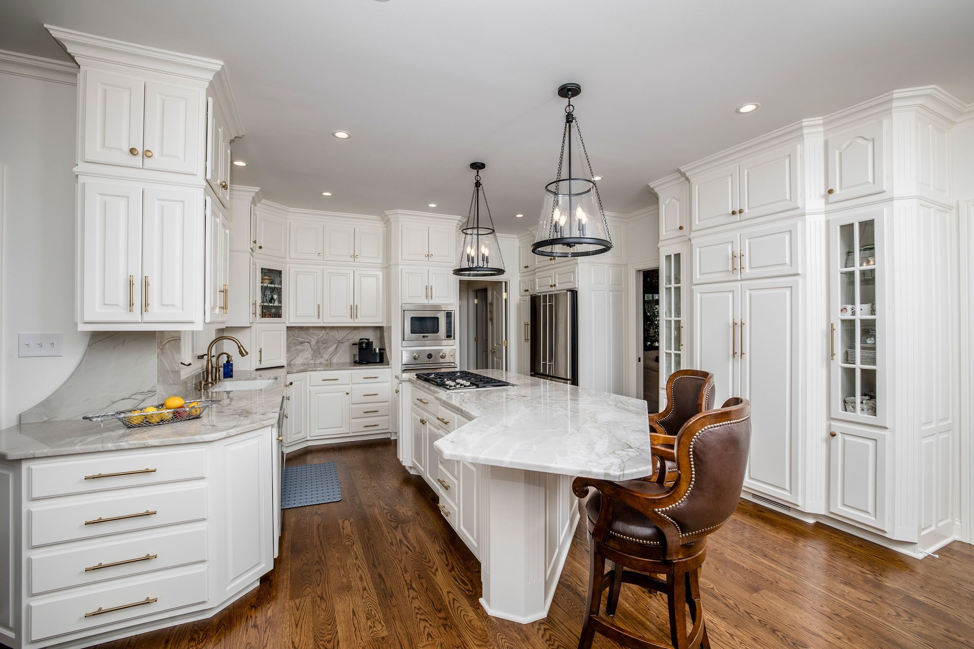 Bright white modern kitchen with island, pendant lights, hardwood floors, and a wooden barstool