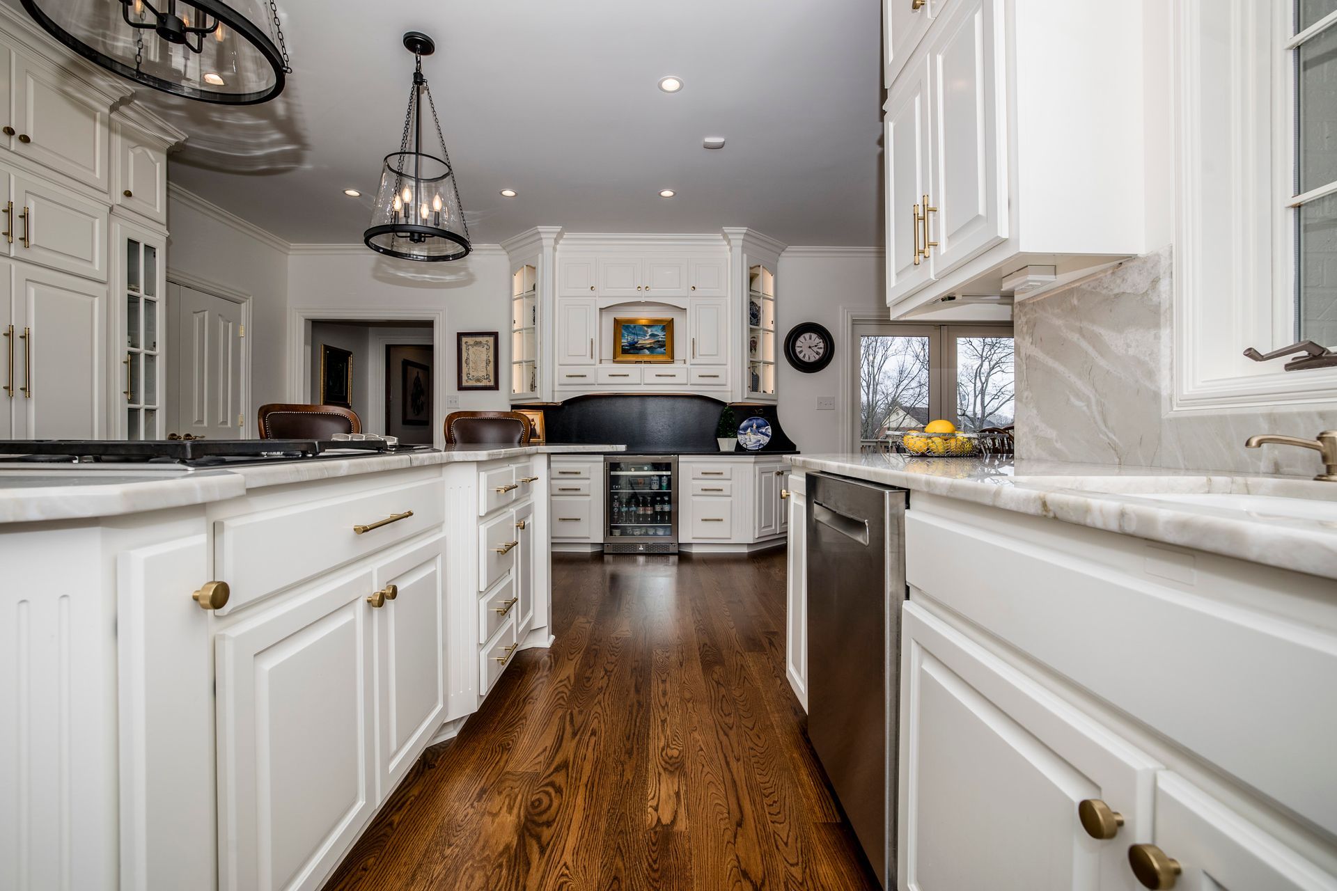 Bright white kitchen with dark wood floors, island, marble countertops, and stainless steel appliances