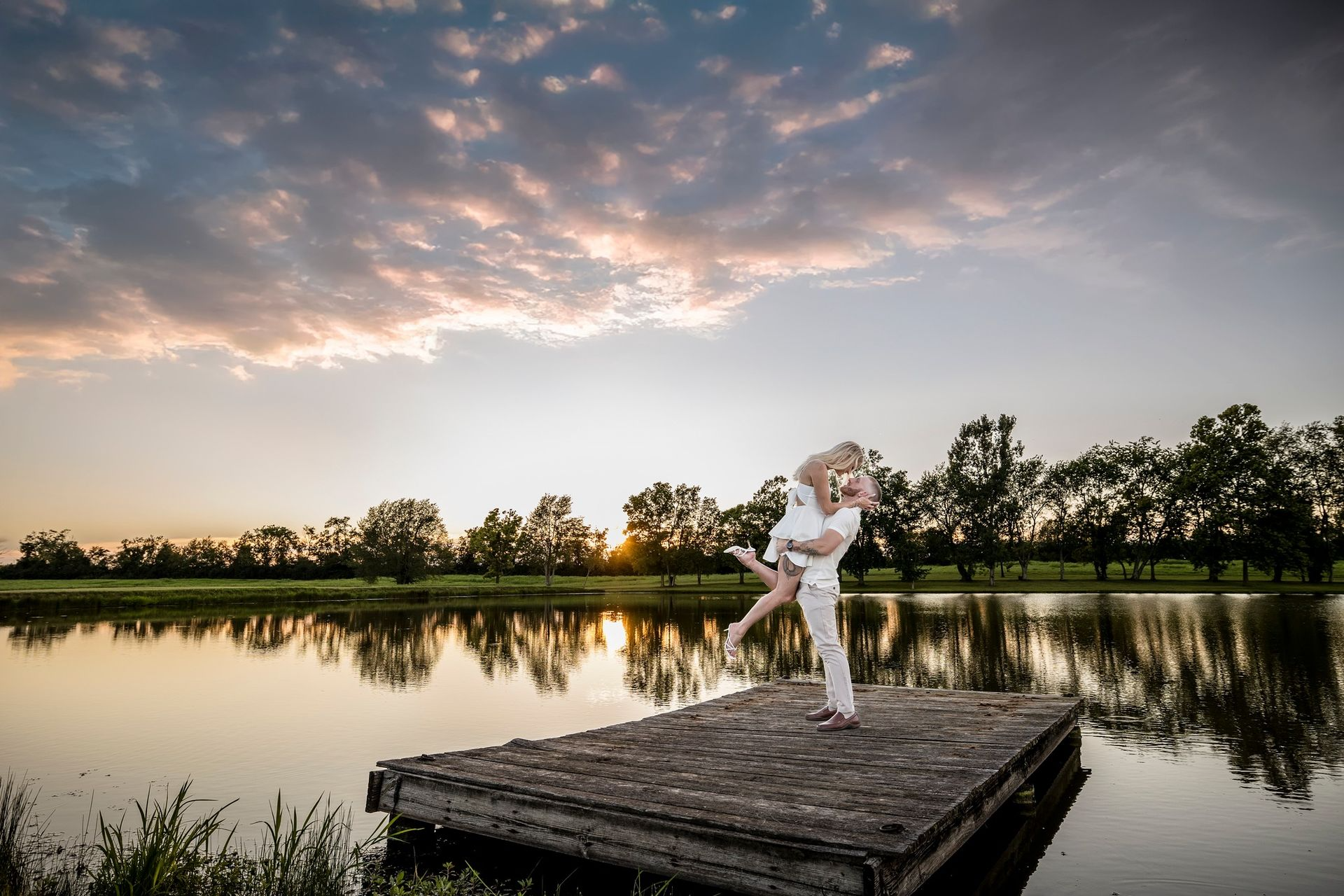 Couple embraces on dock at sunset over a lake.