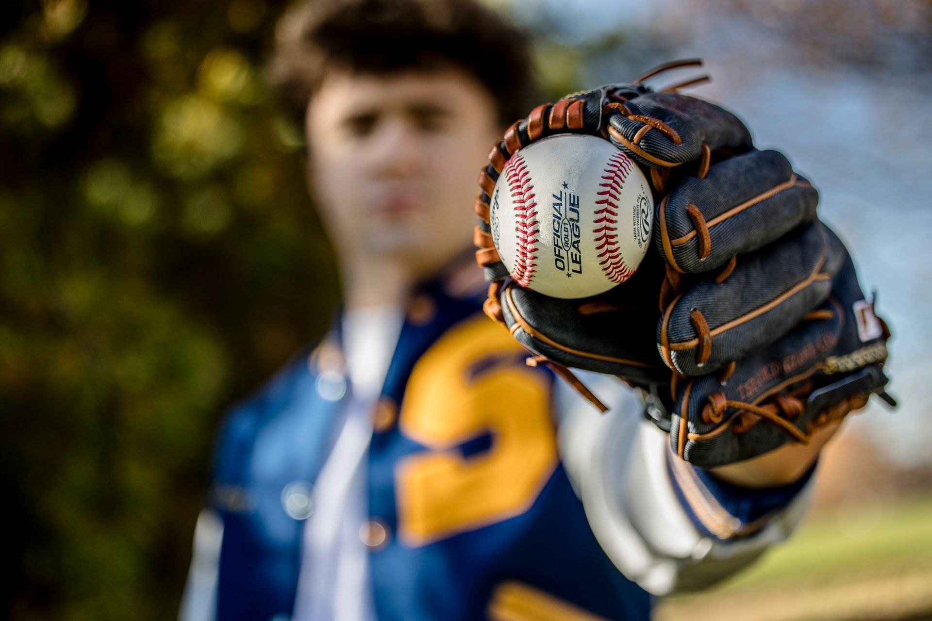 Baseball player in blue jacket holding a baseball in a glove toward the camera