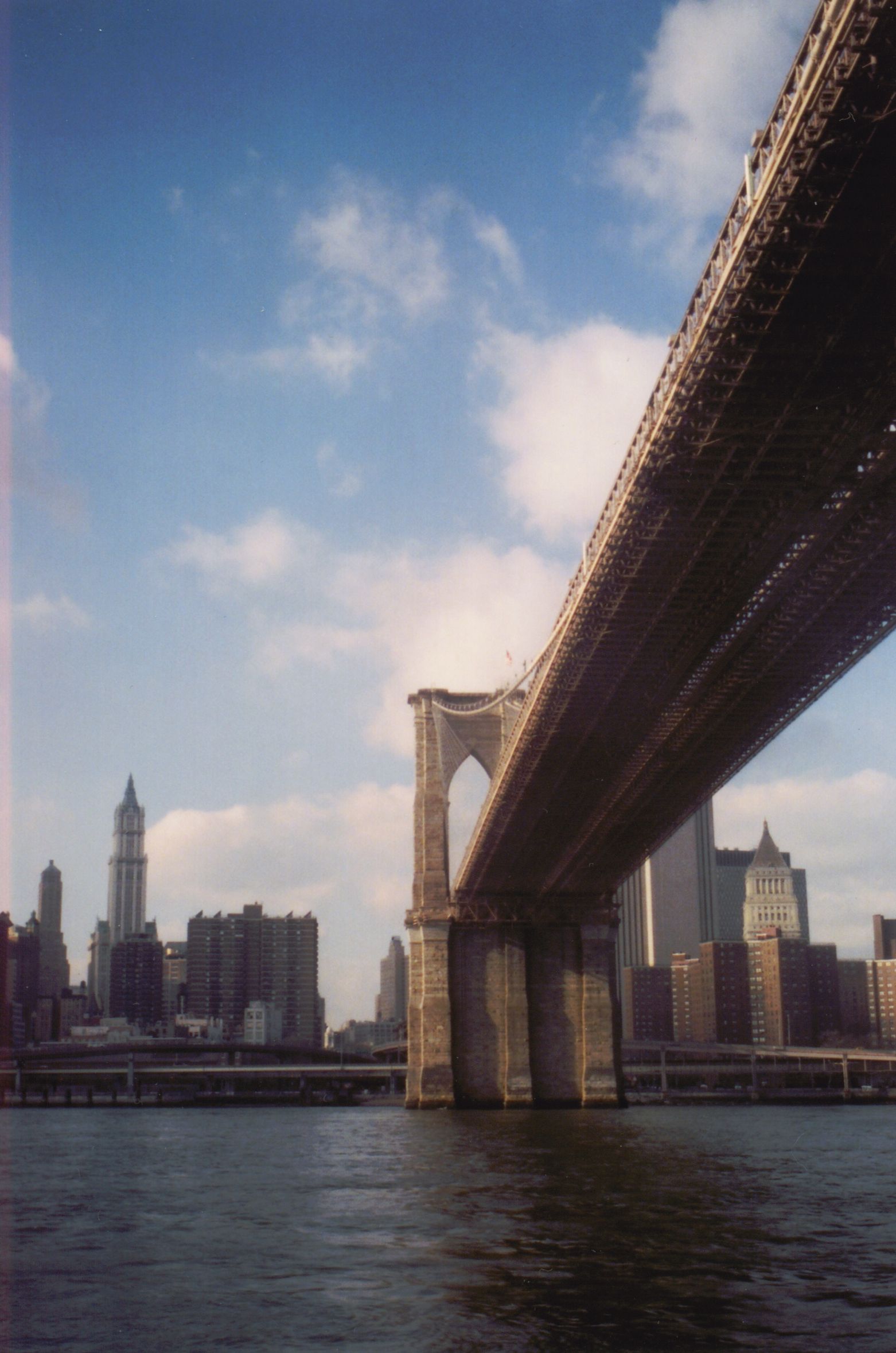 Brooklyn Bridge spanning a river with Manhattan skyline under a blue sky