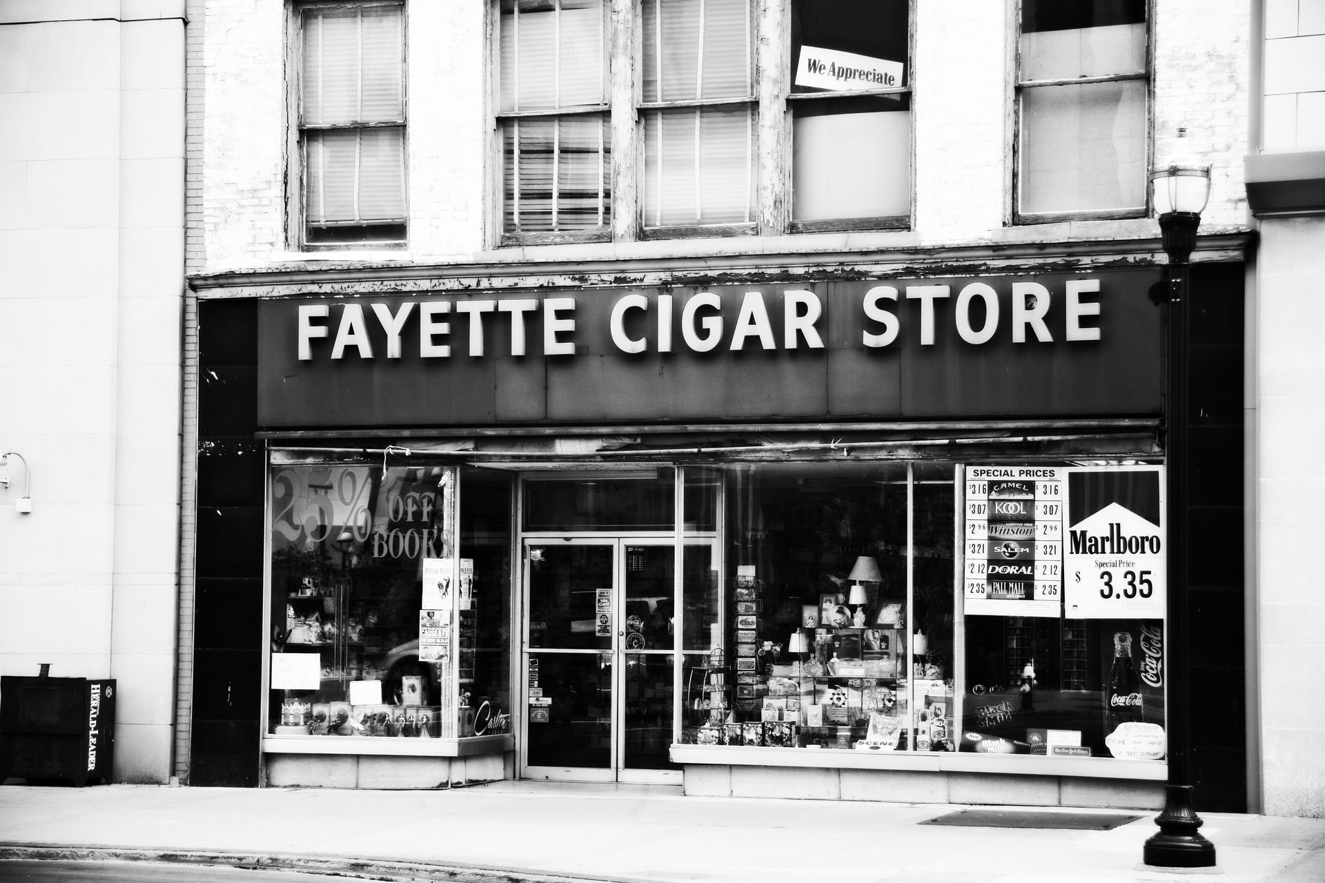 Black-and-white storefront of Fayette Cigar Store with glass windows and signs on a city street