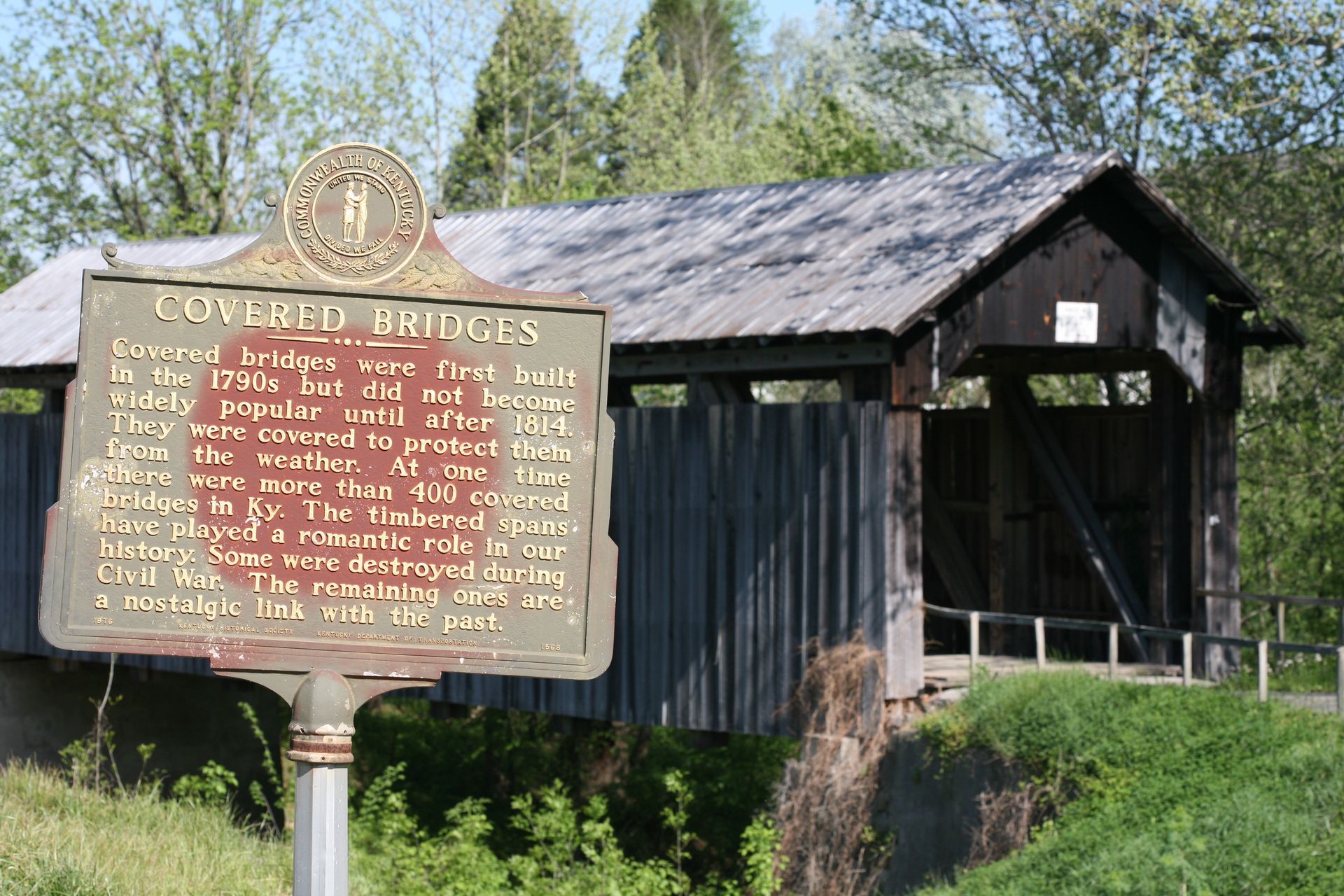 Historic sign in front of a weathered wooden building and trees on a sunny day