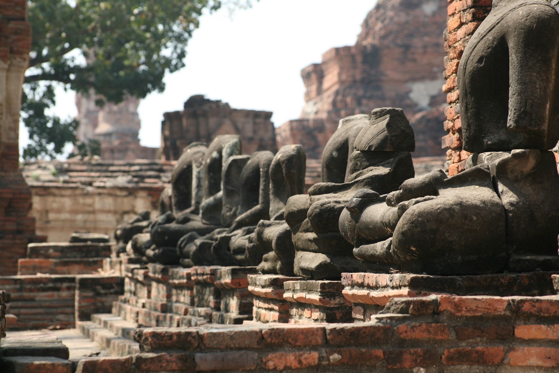 Row of ancient stone Buddha statues on a brick platform at a ruined temple site