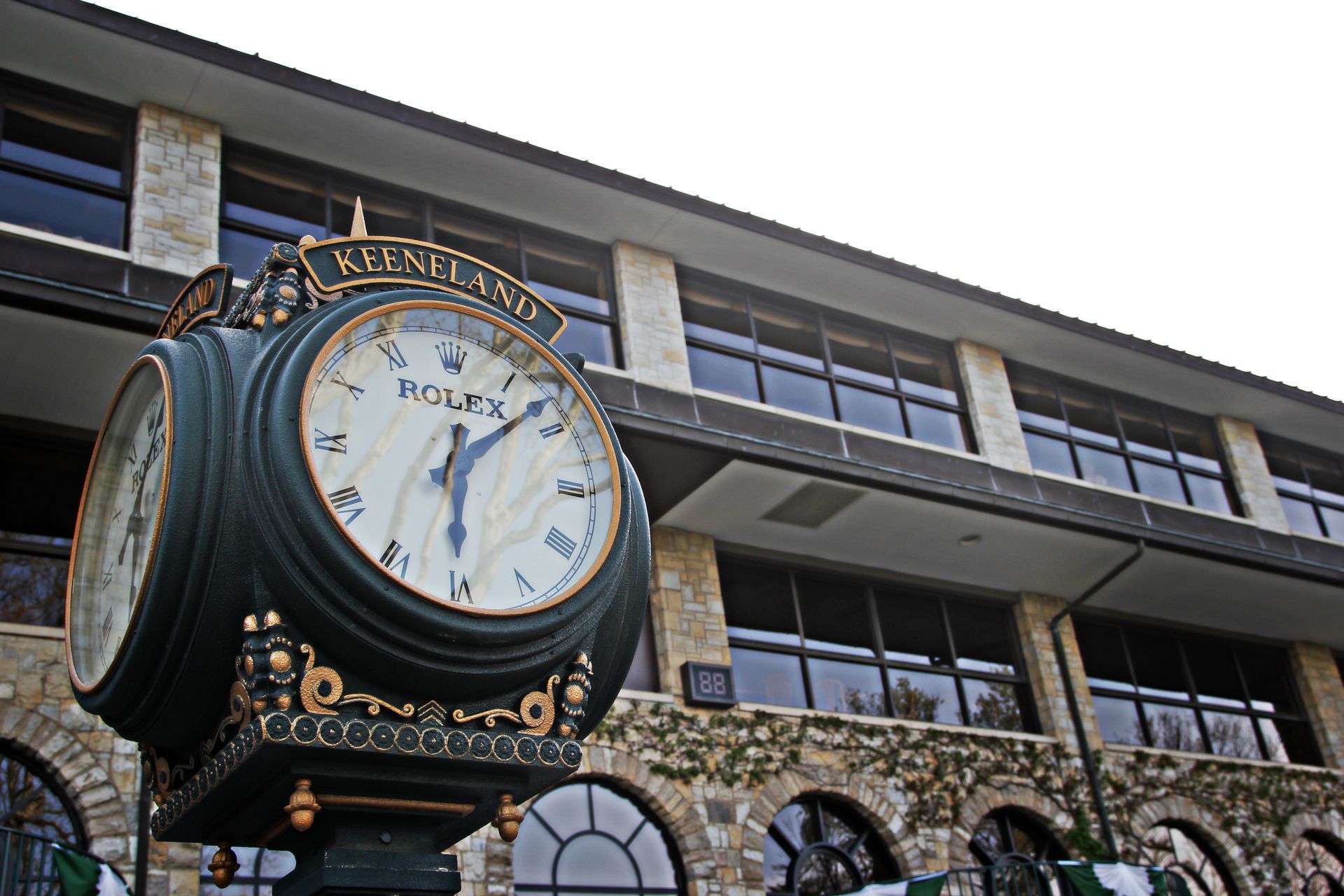 Ornate green Rolex clock in front of a stone building with windows