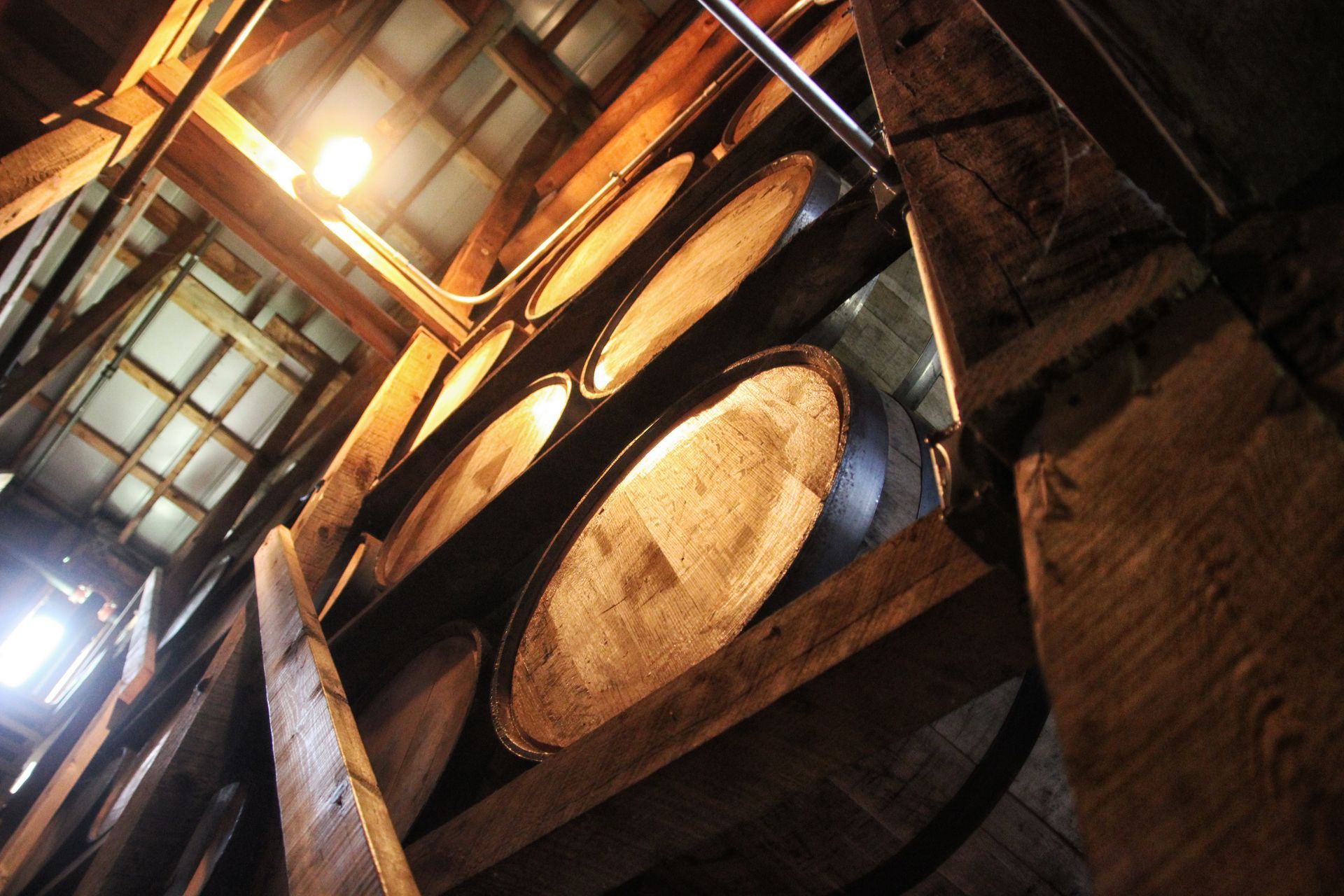 Large wooden barrels stacked in a dimly lit cellar or warehouse, viewed at a steep angle.
