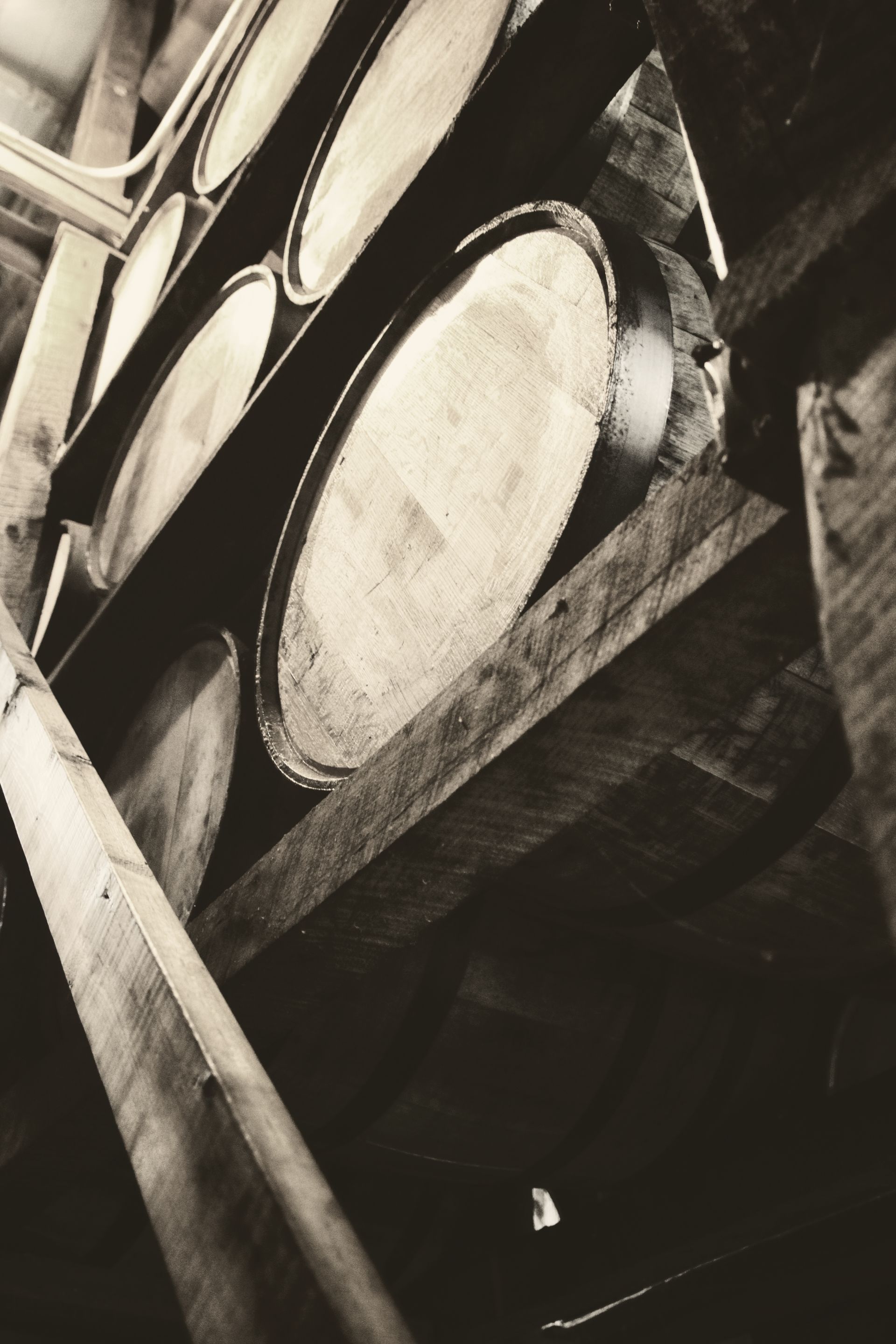 Large wooden barrels stacked on beams in a dim storage cellar.