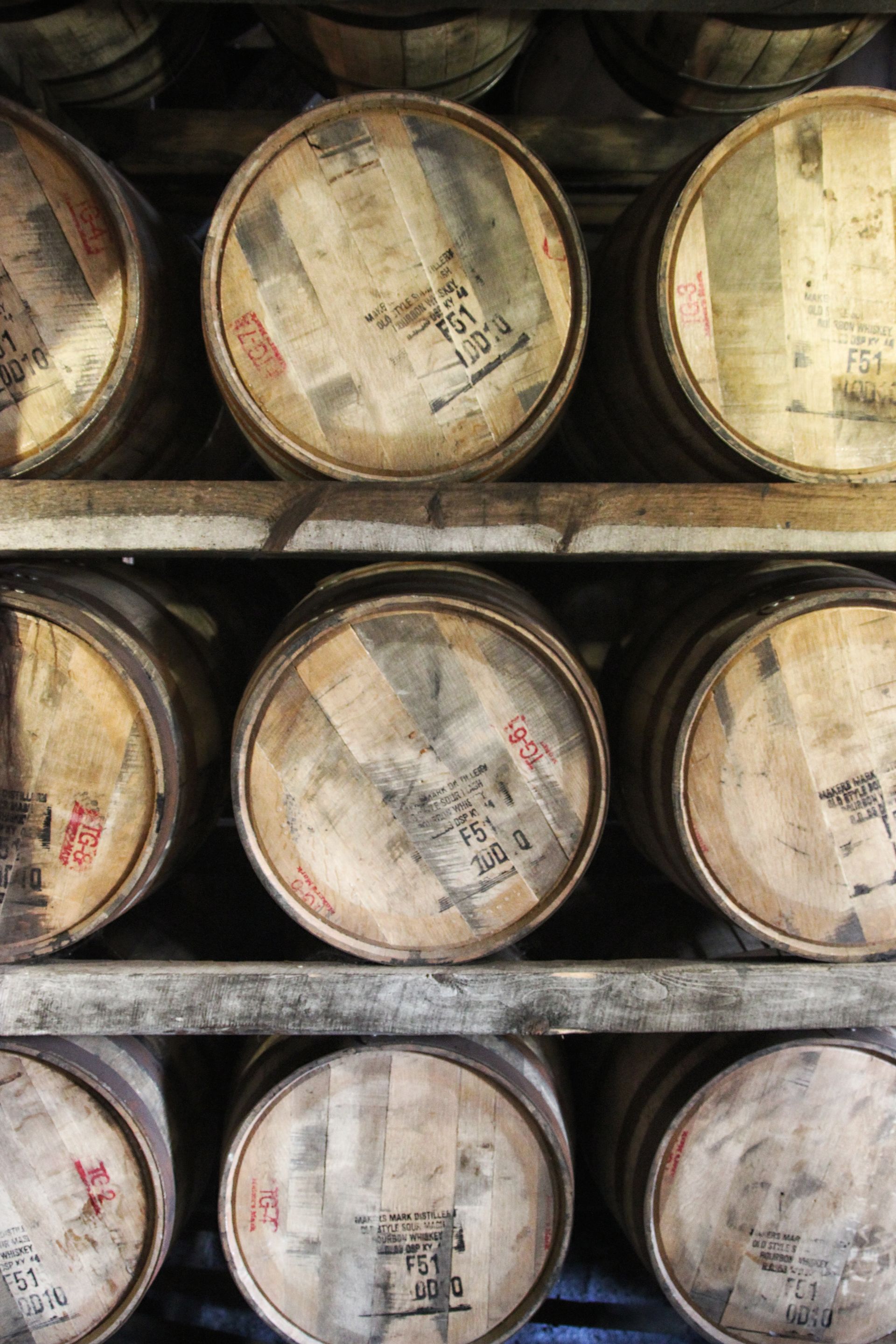 Stacked wooden barrels on metal shelves in a dim storage room.