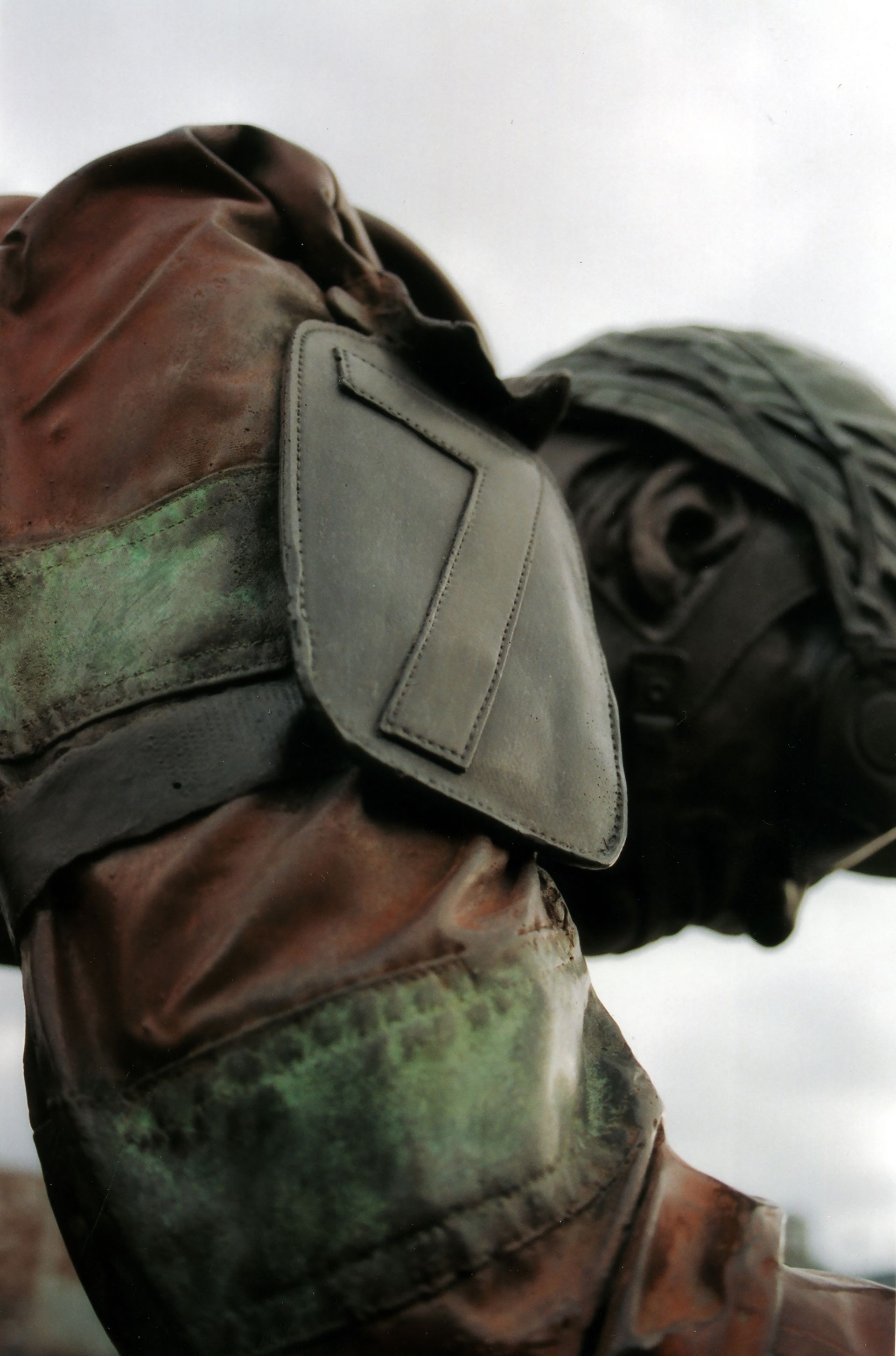Soldier in camouflage jacket and helmet, bent forward against a cloudy sky.
