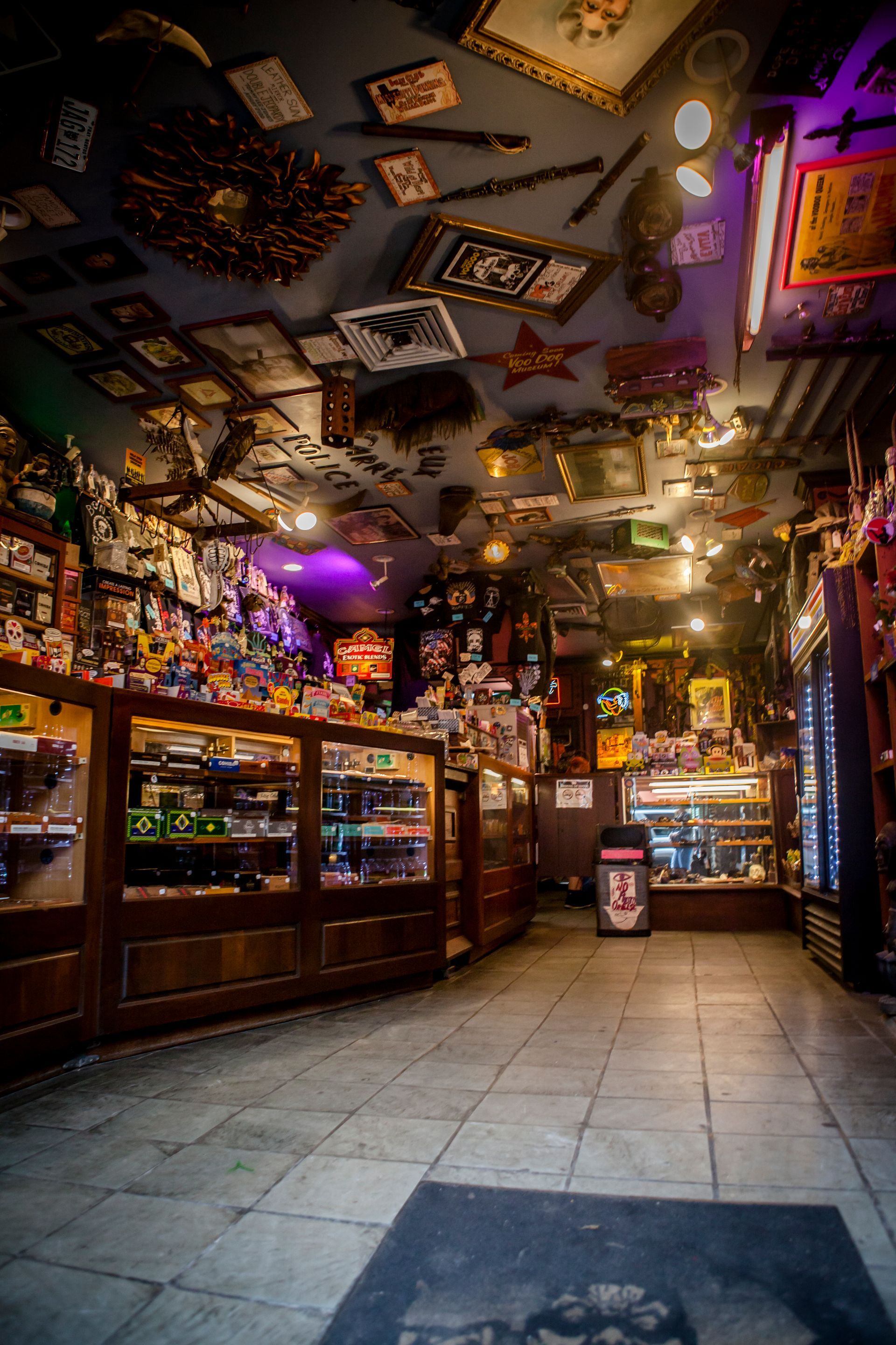 Cozy bar interior with a tiled floor, warm lights, mirrored ceiling decor, and shelves of bottles and snacks