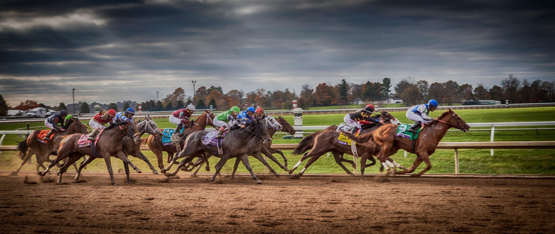 Horse race with jockeys on colorful thoroughbreds kicking up dirt on a track under cloudy skies