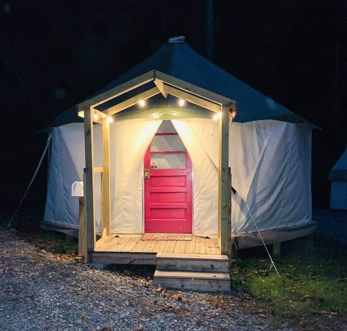 Small lit cabin or yurt with a bright pink door at night