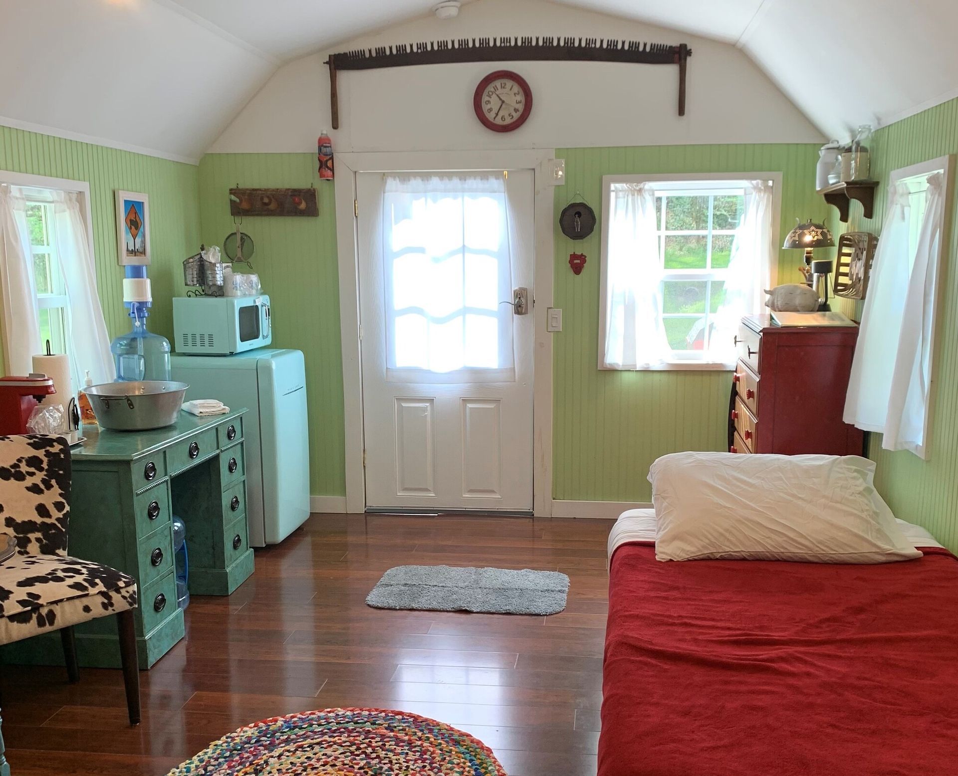 Cozy pastel living room with white door, turquoise cabinet, red couch, and wooden floor.