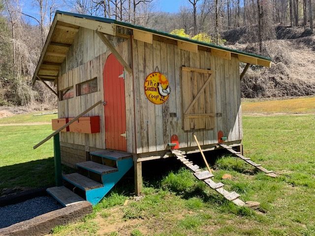 Rustic wooden shed with red doors and ramps on a grassy hillside under a clear sky