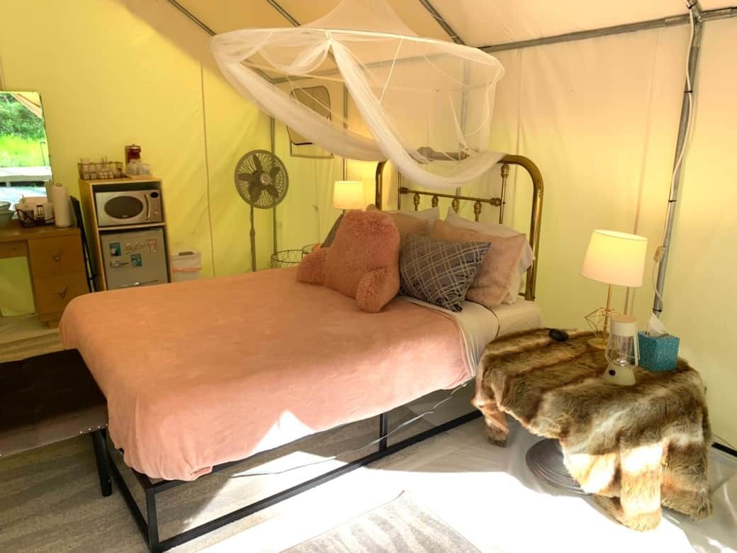 Canopy bed with pink bedding, bedside lamps, and a fan in a cozy tented bedroom