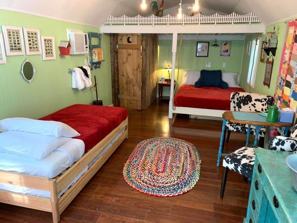 Cozy bedroom with two beds, green walls, colorful rug, and wooden flooring