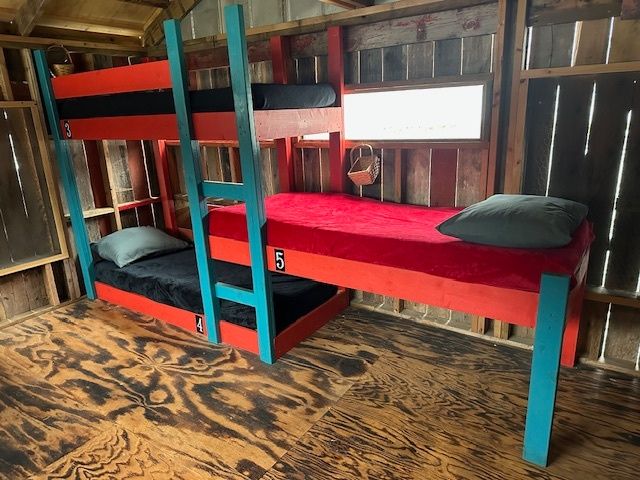 Two bunk beds with red and blue frames in a rustic wooden room with mattresses and pillows