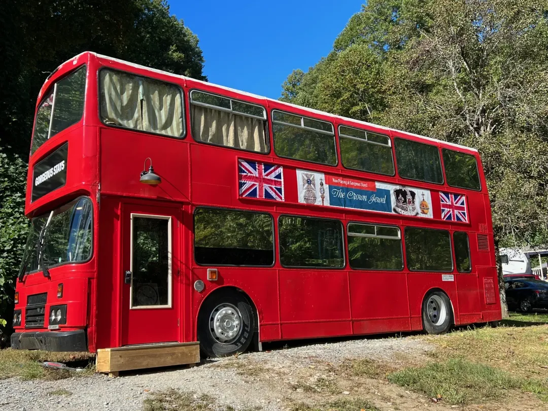 Red double-decker bus painted with Union Jack flags, parked outdoors under a blue sky.