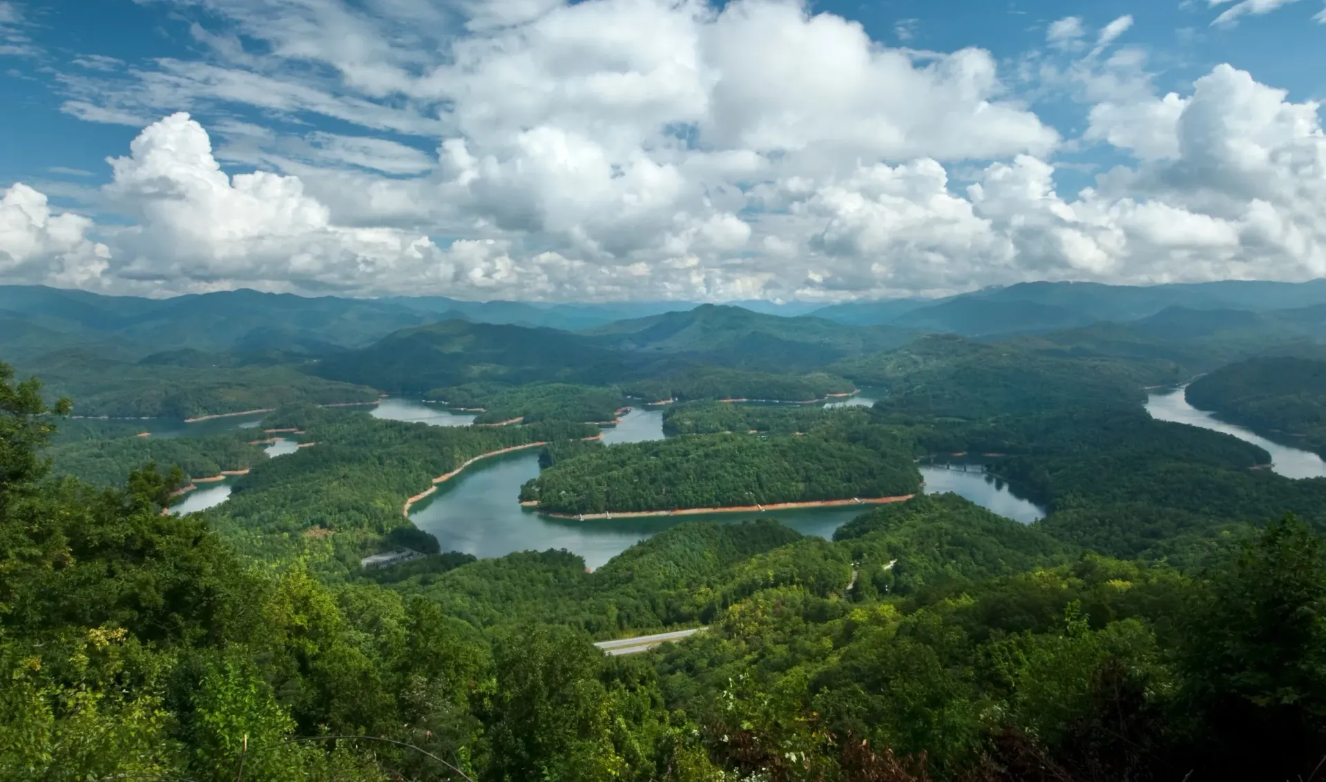 Panoramic green valley with a winding river, forested hills, and cloudy blue sky