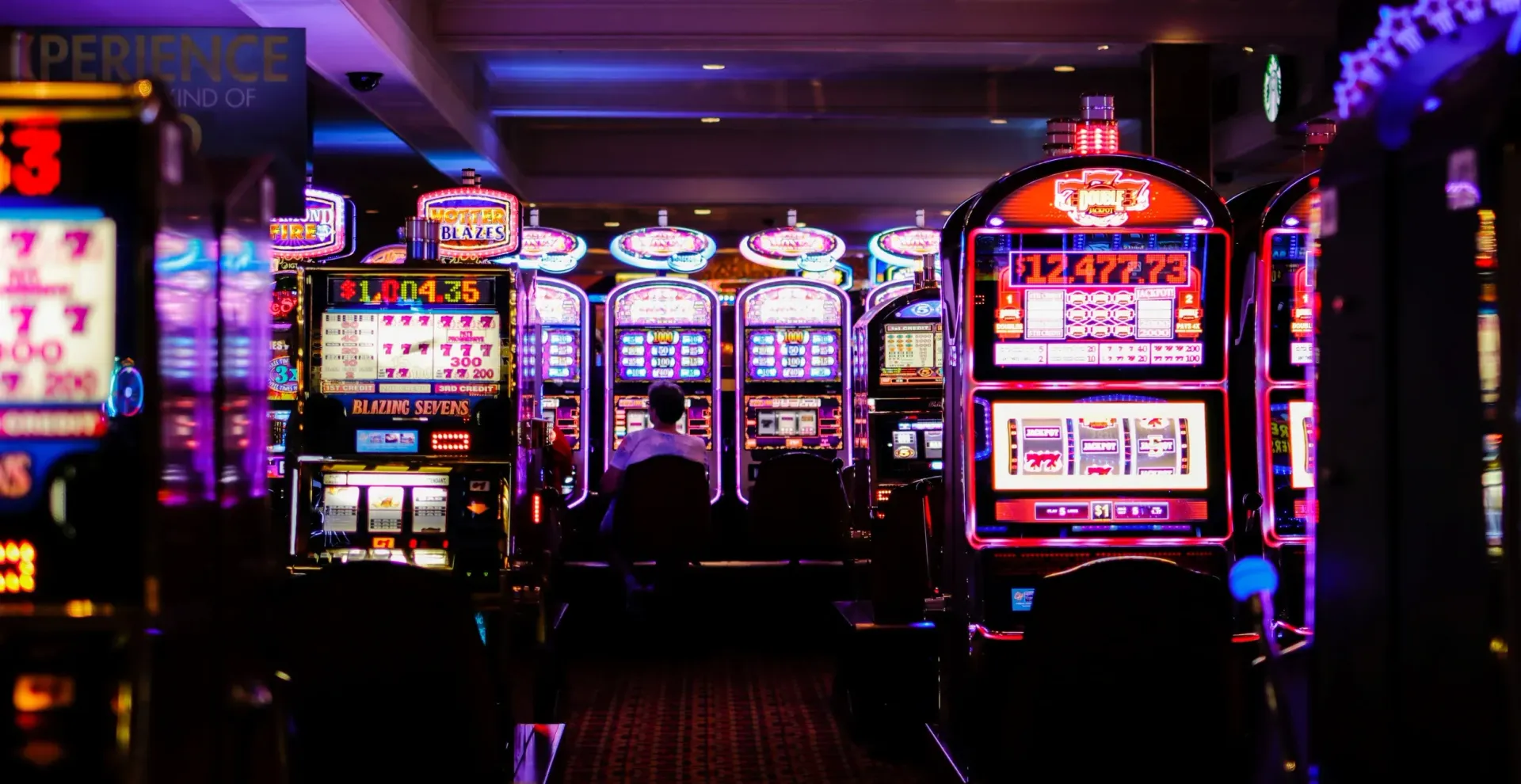 Neon-lit casino aisle with rows of slot machines glowing in purple, red, and blue.